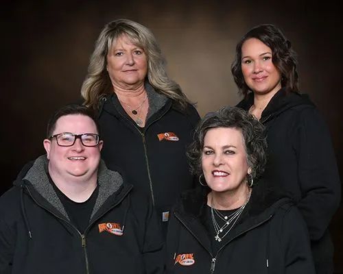 Four people in black jackets, smiling, posing together against a brown backdrop.