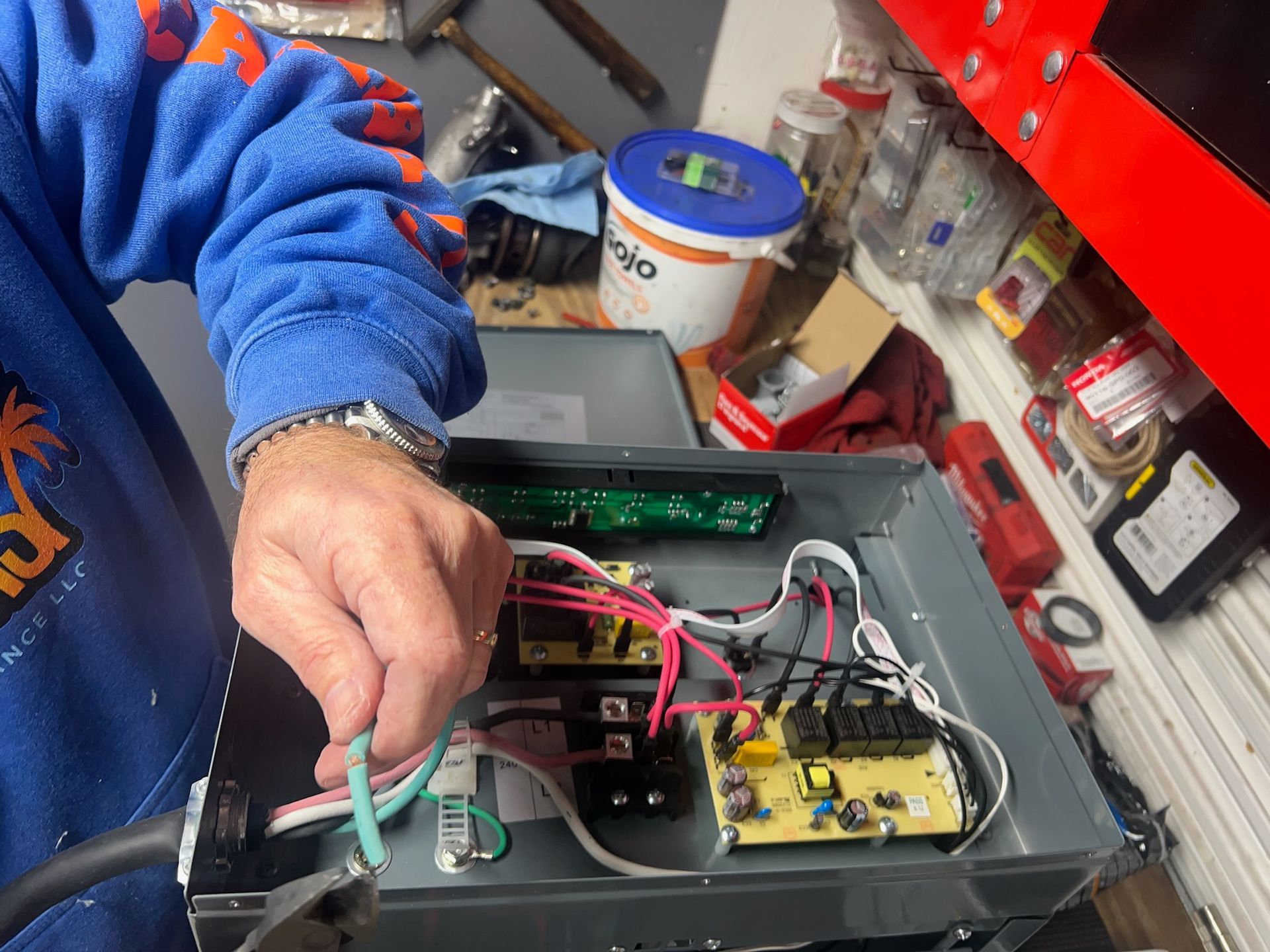 Person wiring electrical components inside a metal box.  Green wire held with hand; various wires and circuit boards visible.