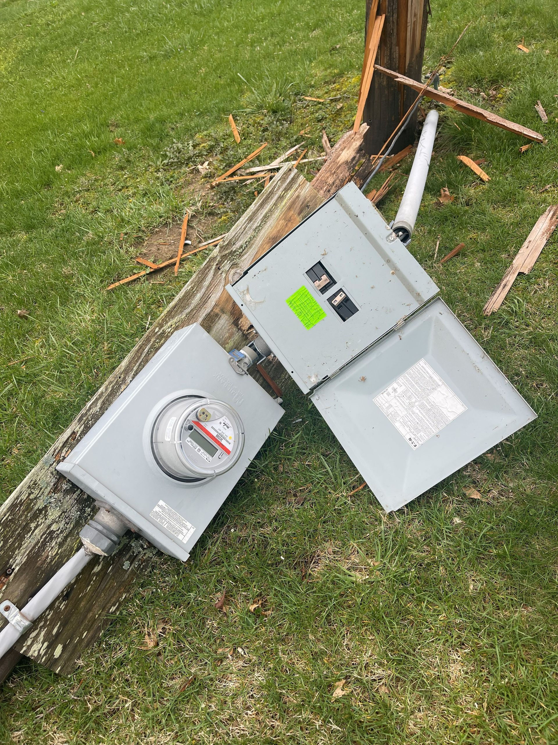 Utility meter box and conduit are damaged, lying on grass next to a broken utility pole.