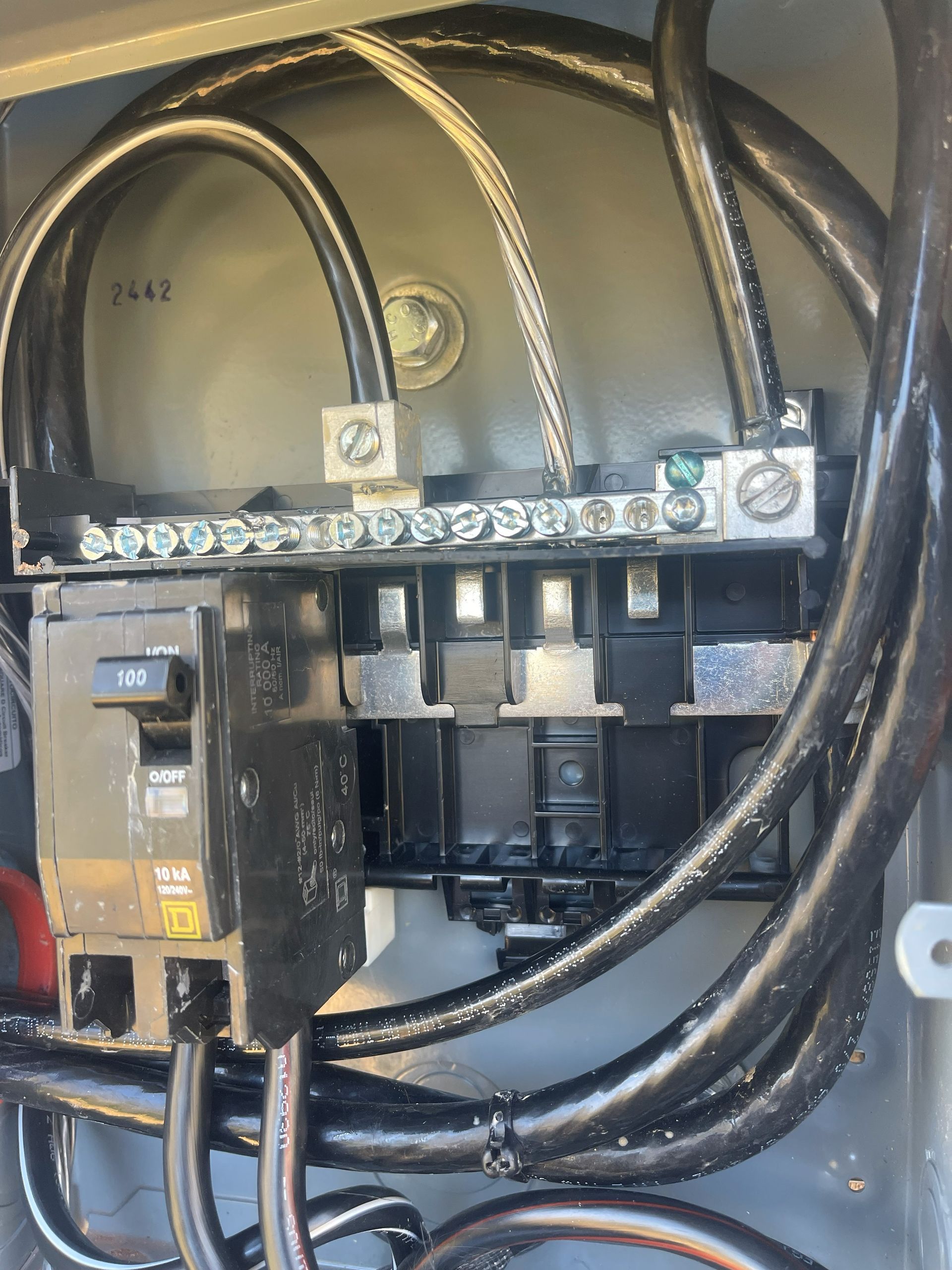Electrical panel with black wires, circuit breakers, and grounding bar.