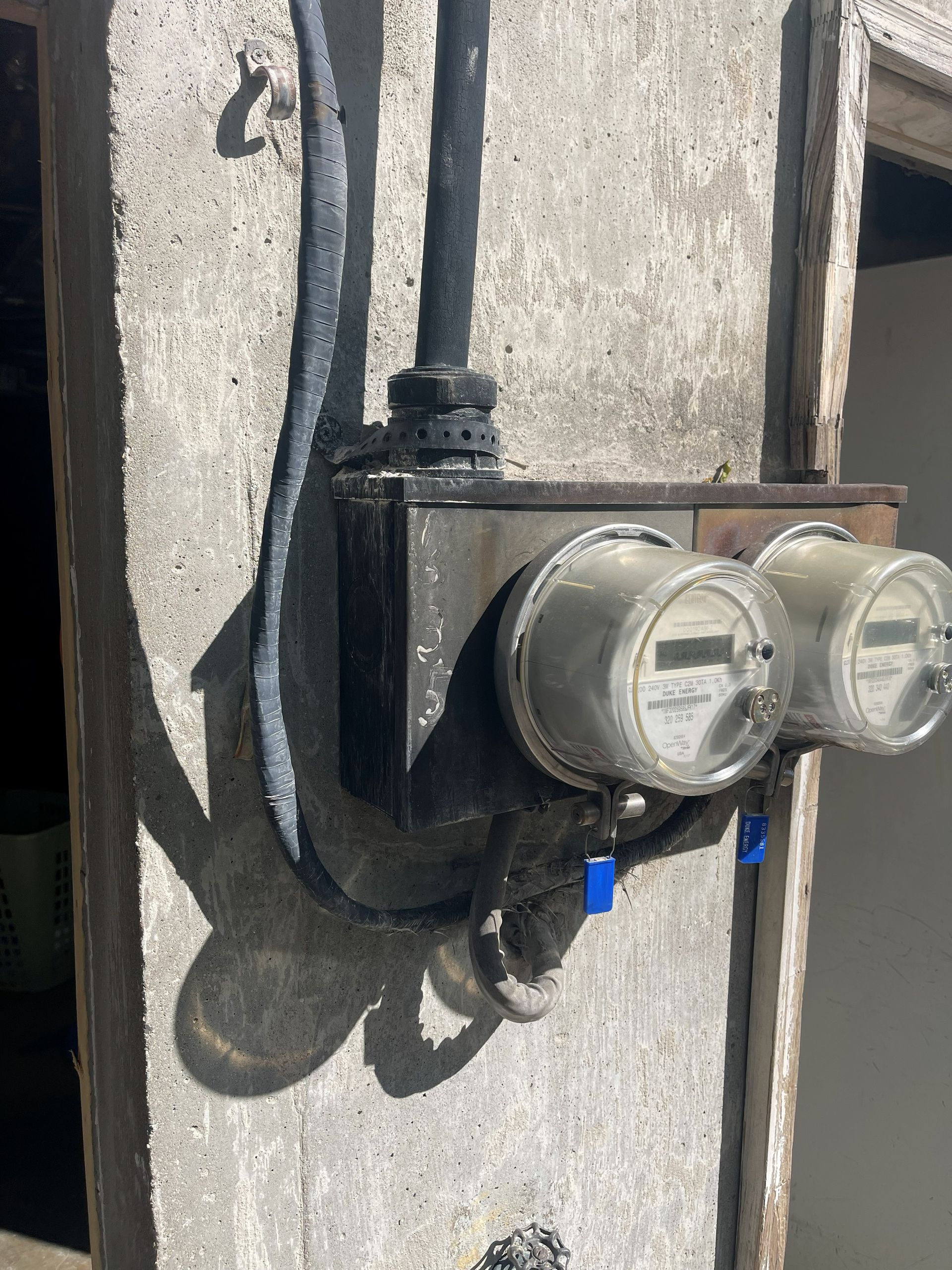 Two electric meters mounted on a concrete column, with black wires and blue connectors.