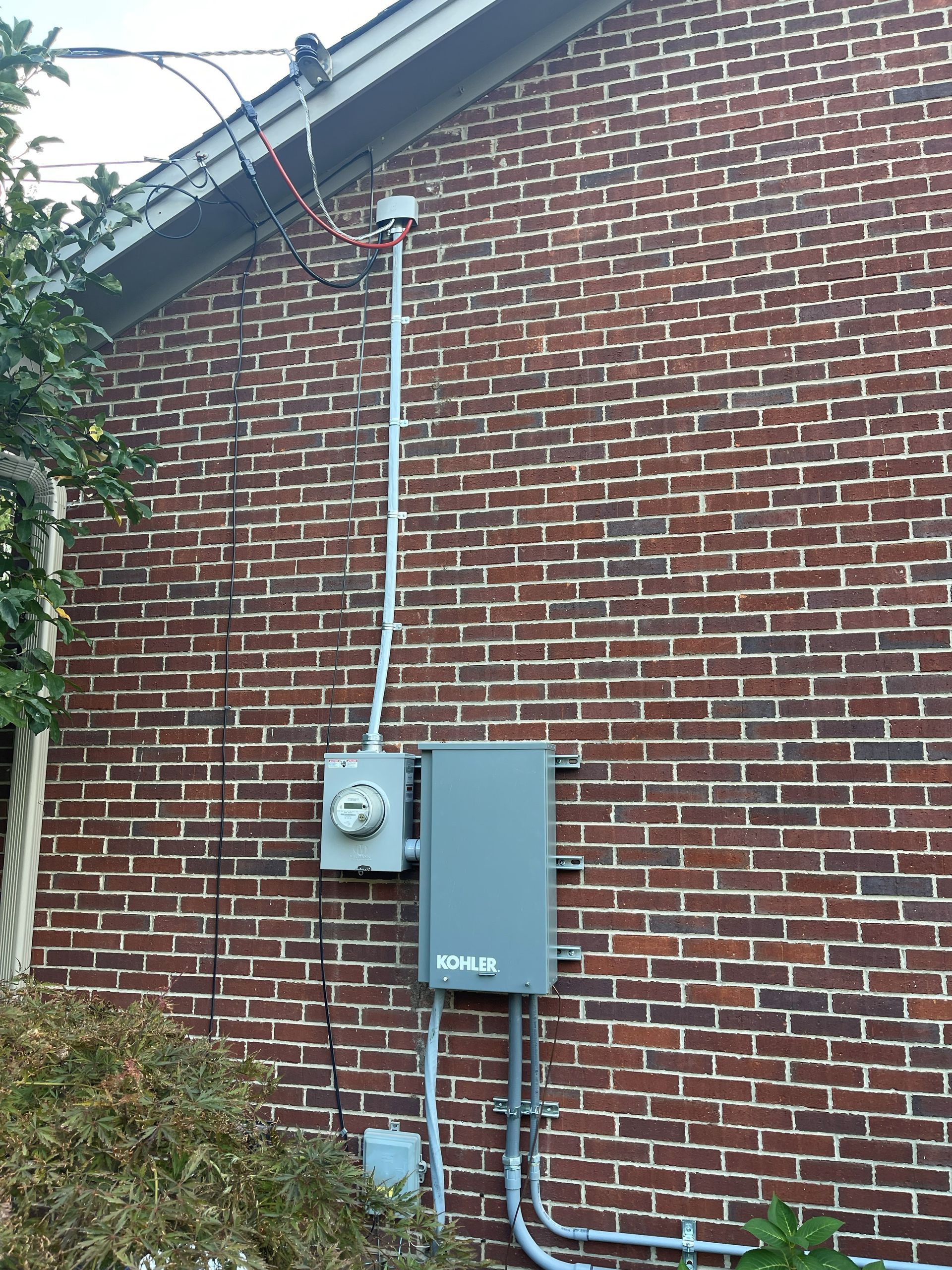 Brick building exterior with gray electrical components, including a meter and box, attached to the wall.