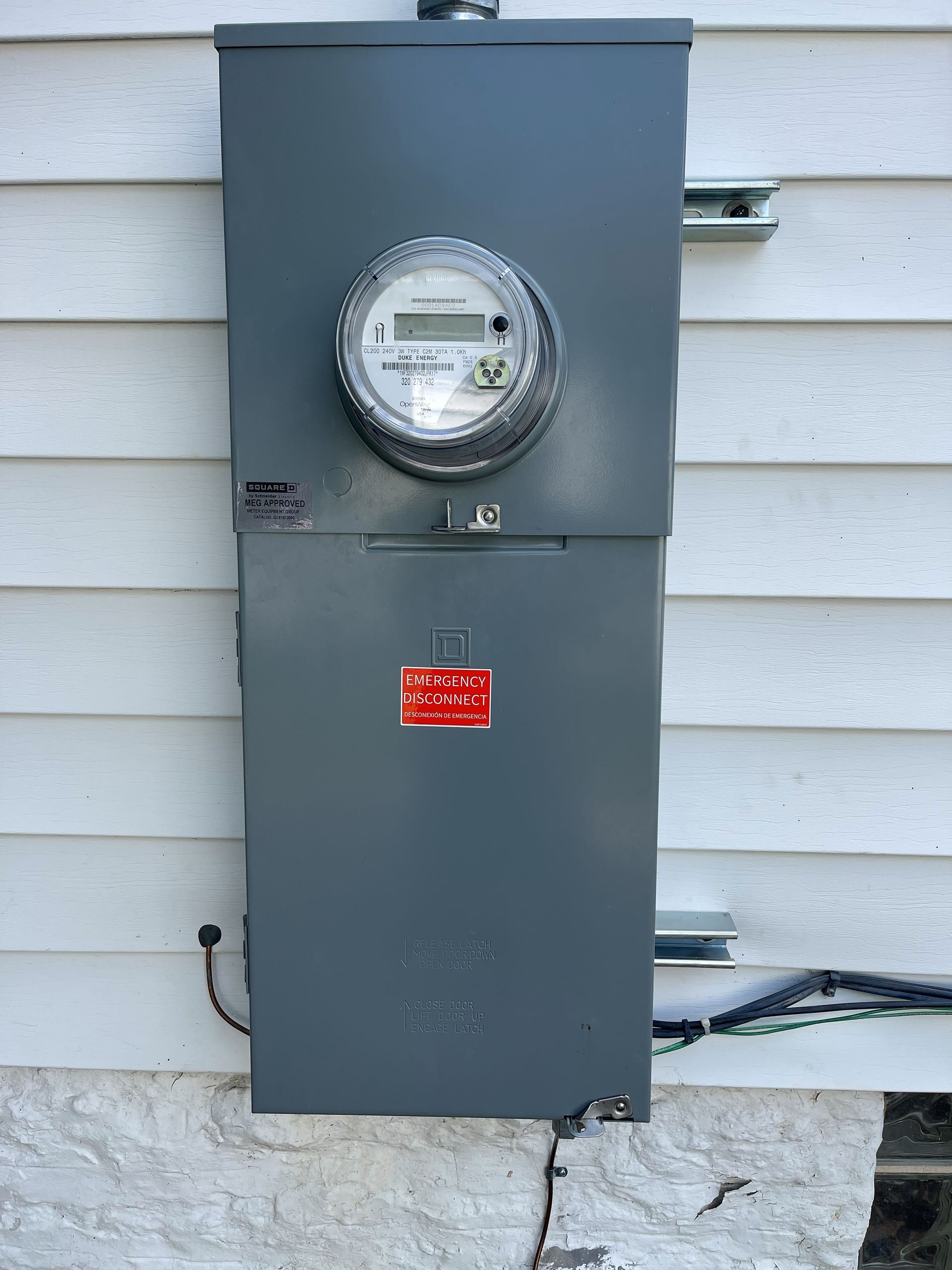 Gray electrical meter box on a white-sided house.
