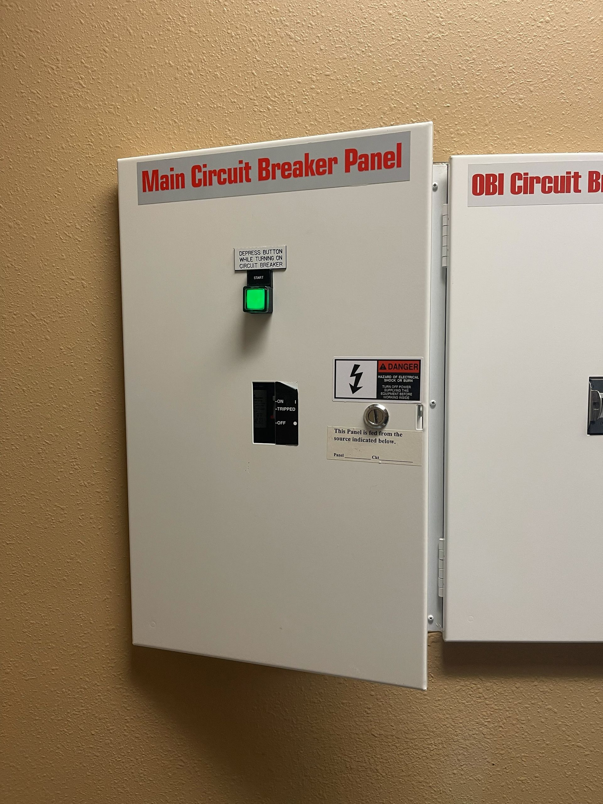 White main circuit breaker panel with green light, mounted on a tan wall.