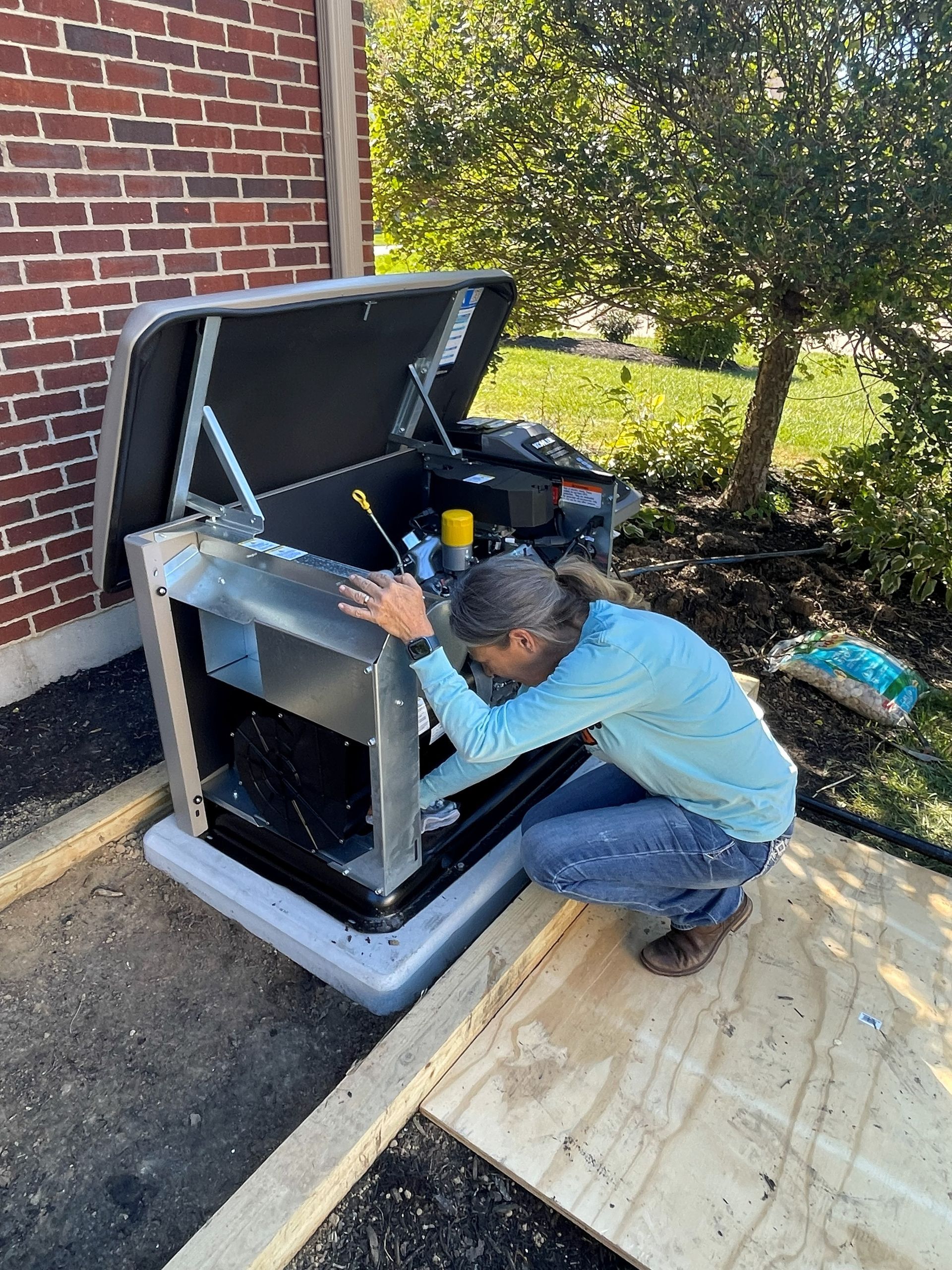 Person working on a generator next to a brick building. The generator is on a concrete pad.