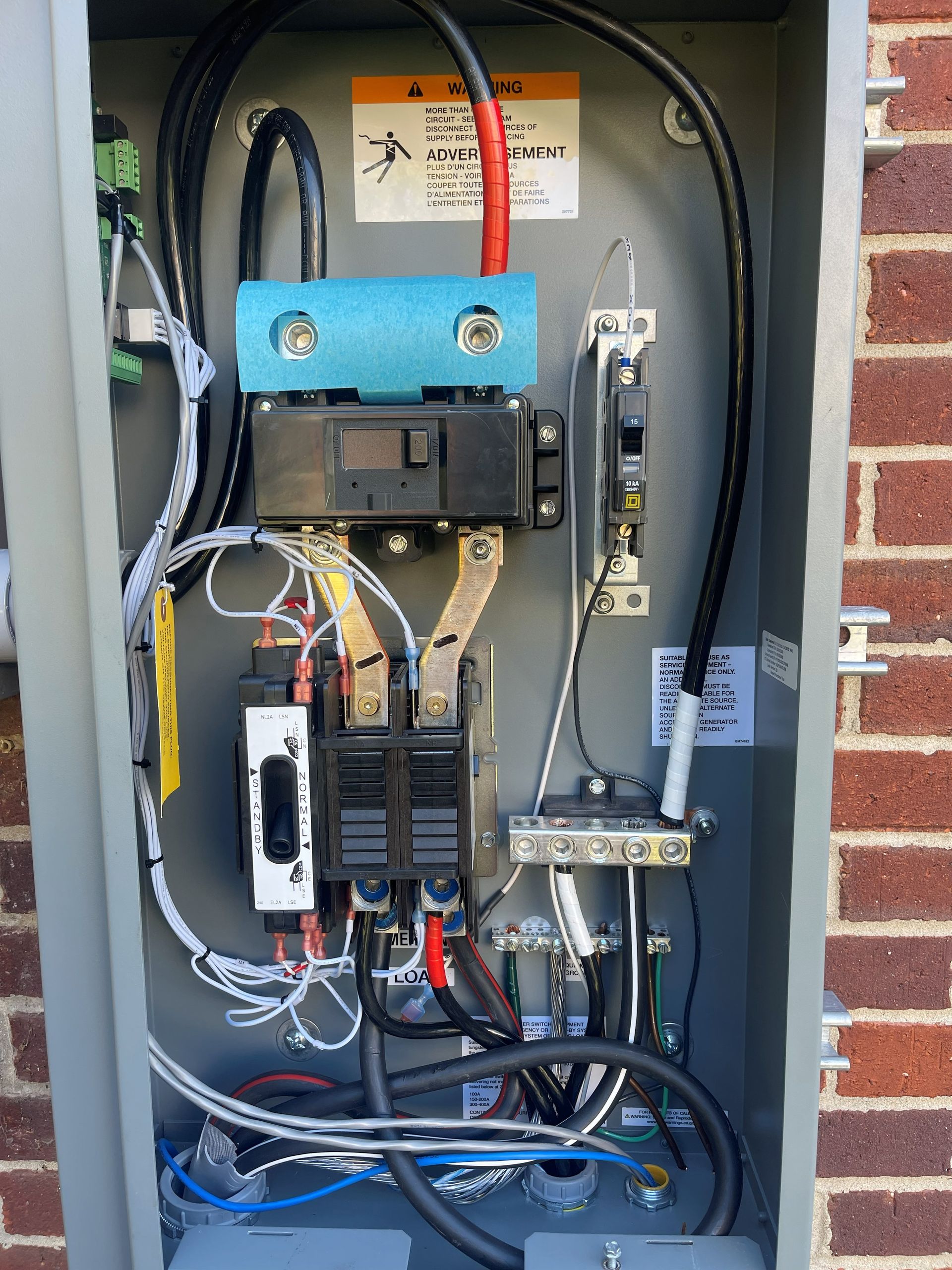 Electrical panel with wires and circuit breakers mounted on brick wall.
