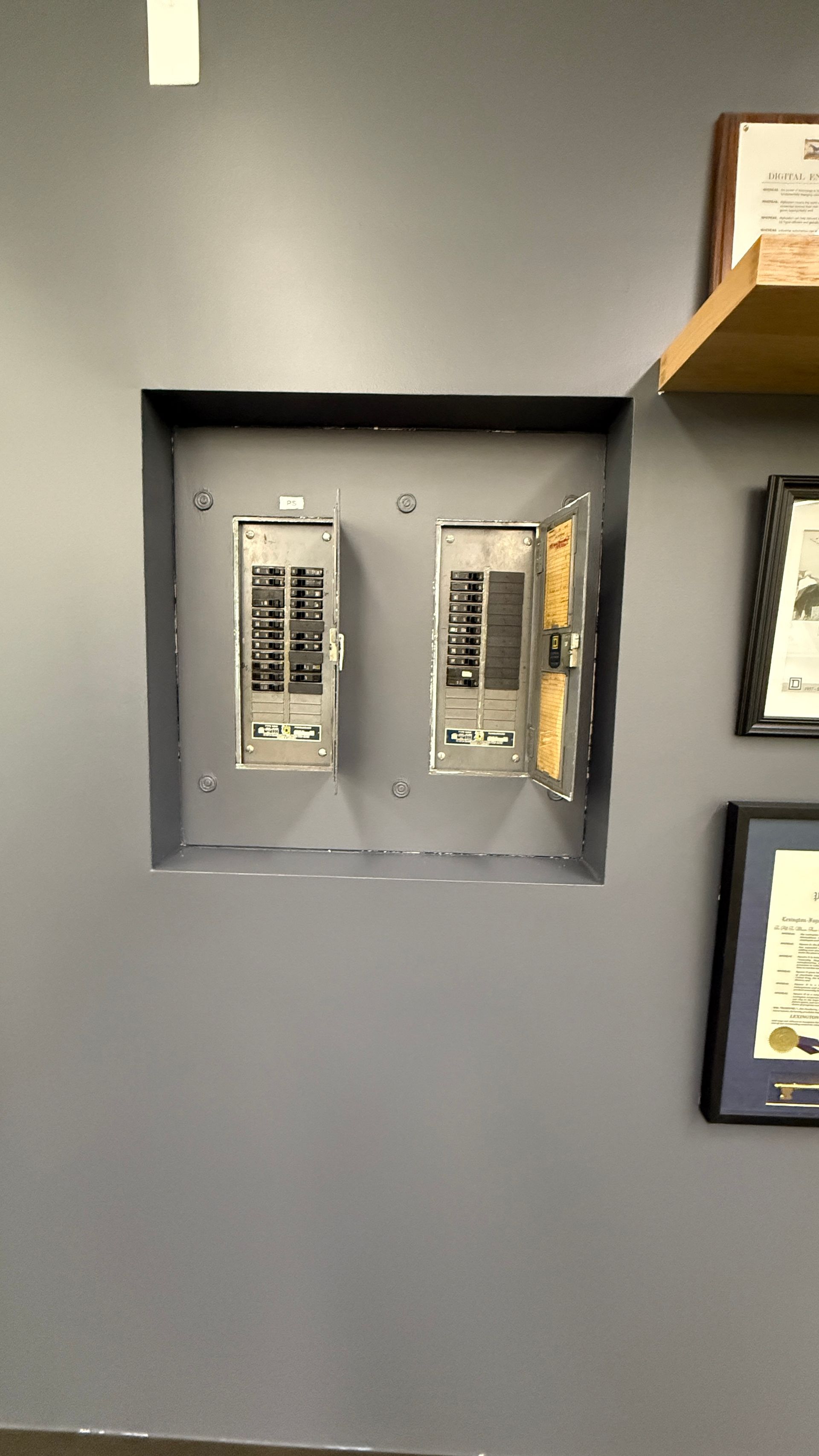 Two electrical panels recessed in a gray wall, one open, the other closed.