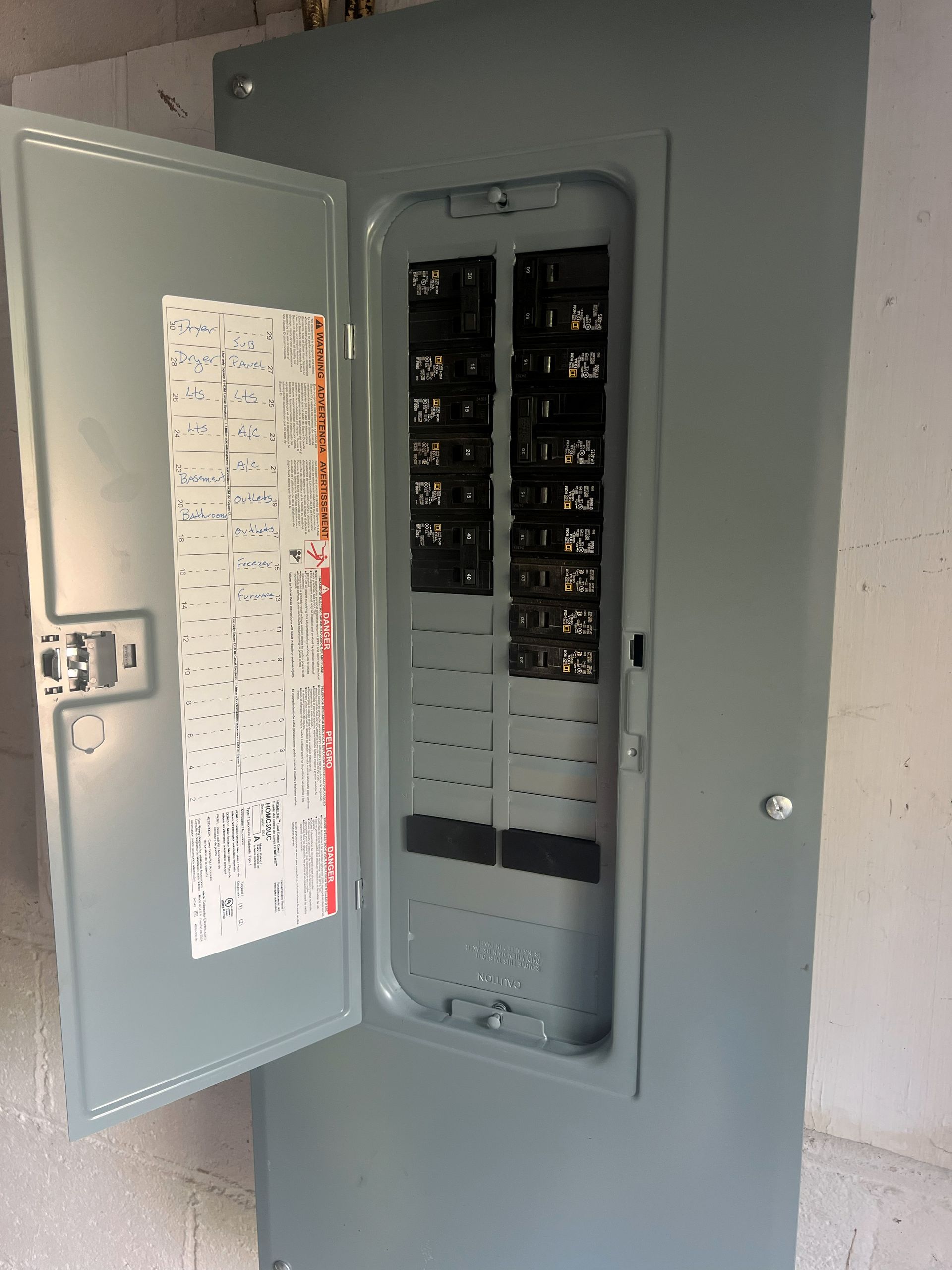 Open gray electrical breaker panel on a wall, showing numerous black switches.
