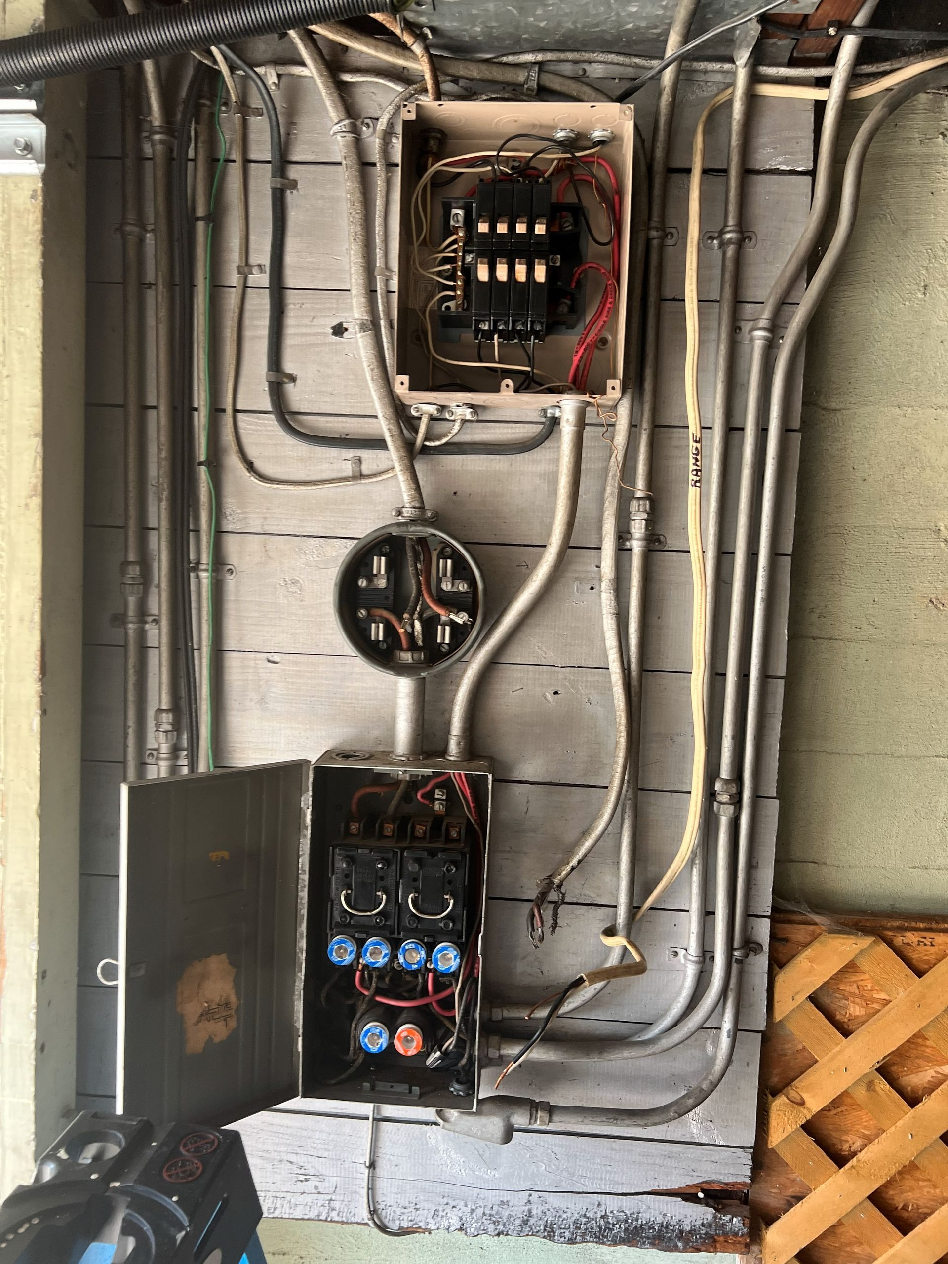 Electrical panel with conduits attached to a gray wooden wall.