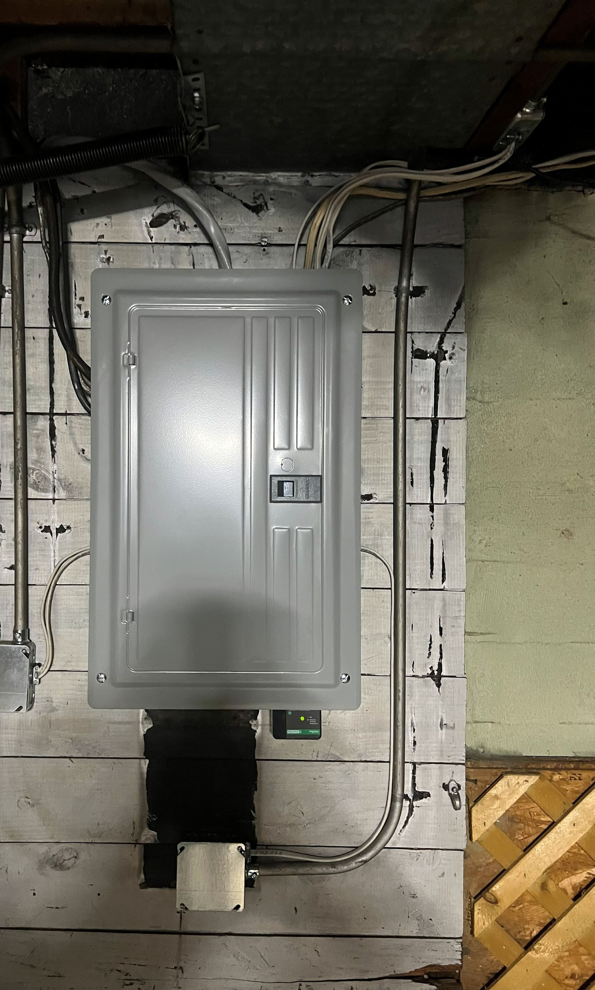Electrical panel mounted on a wooden wall. Gray panel, conduit, and wiring visible.