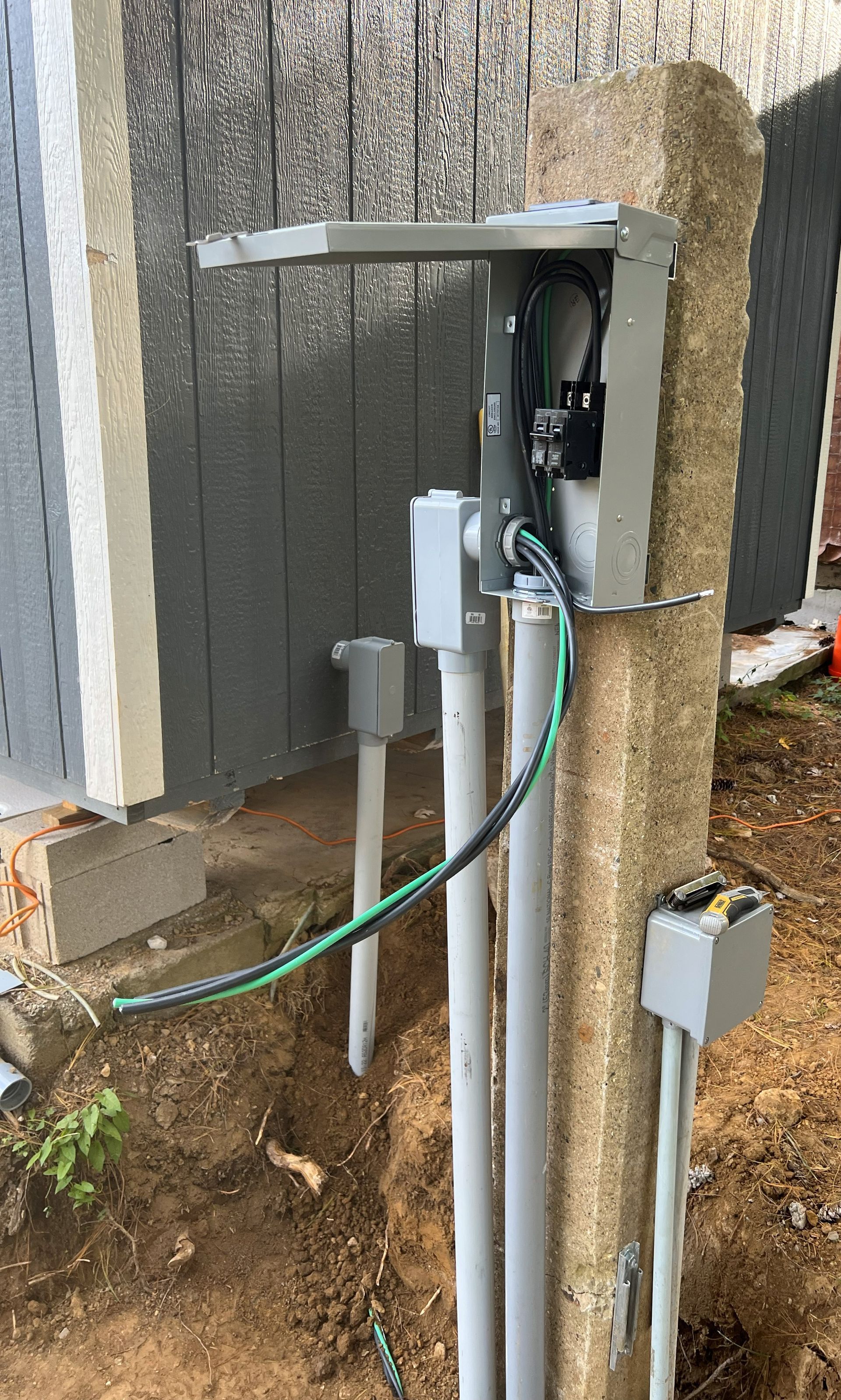 Electrical panel and conduits mounted on a concrete column near a building's exterior.