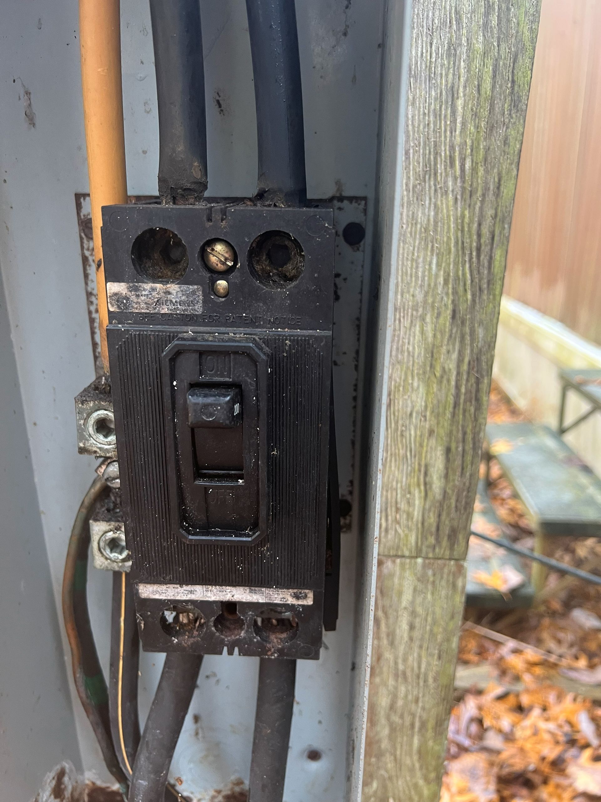 Black circuit breaker in an outdoor electrical box; wires attached, dark residue present.