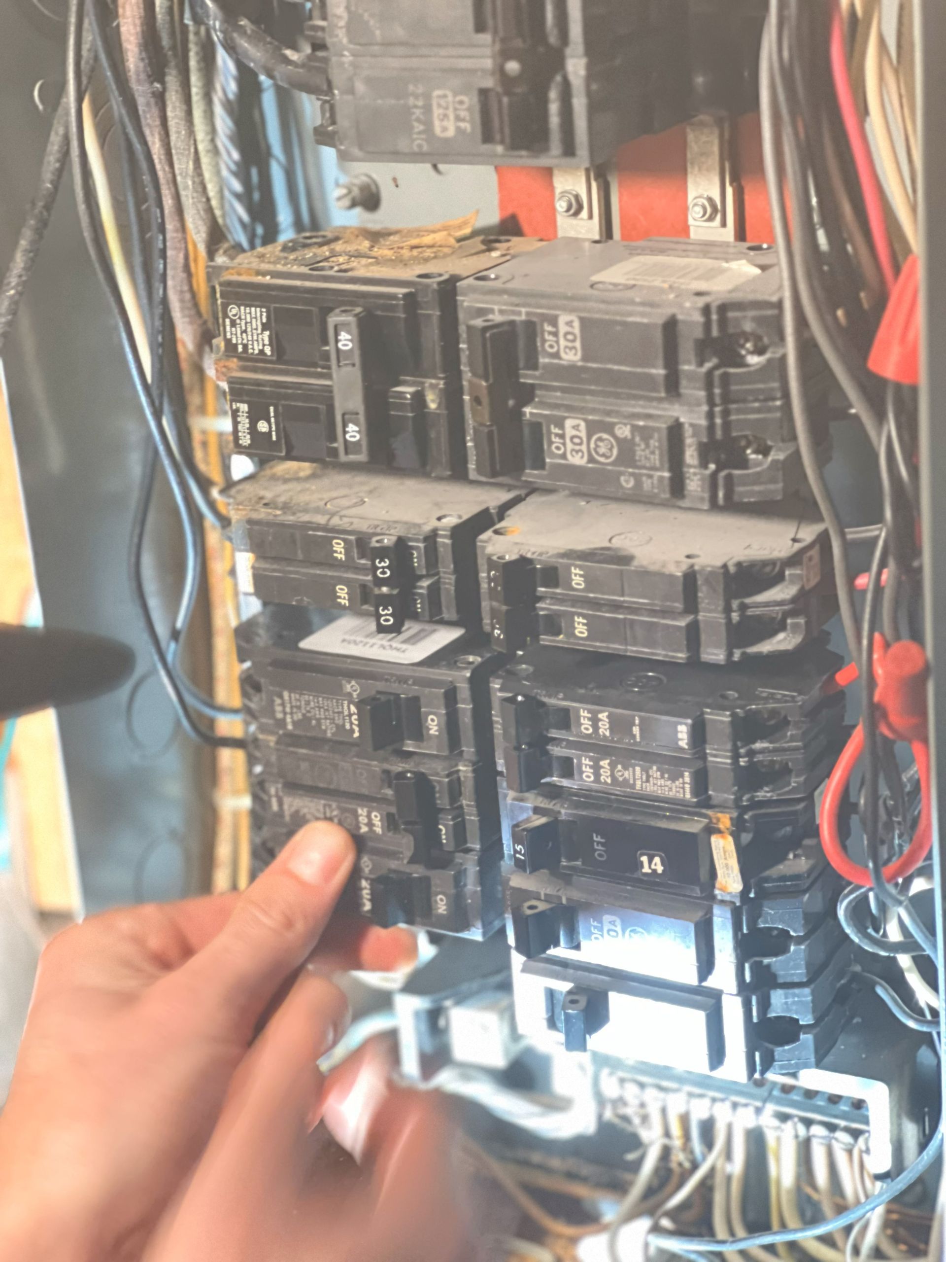 Hand removing a circuit breaker from an electrical panel, wires visible, dusty setting.