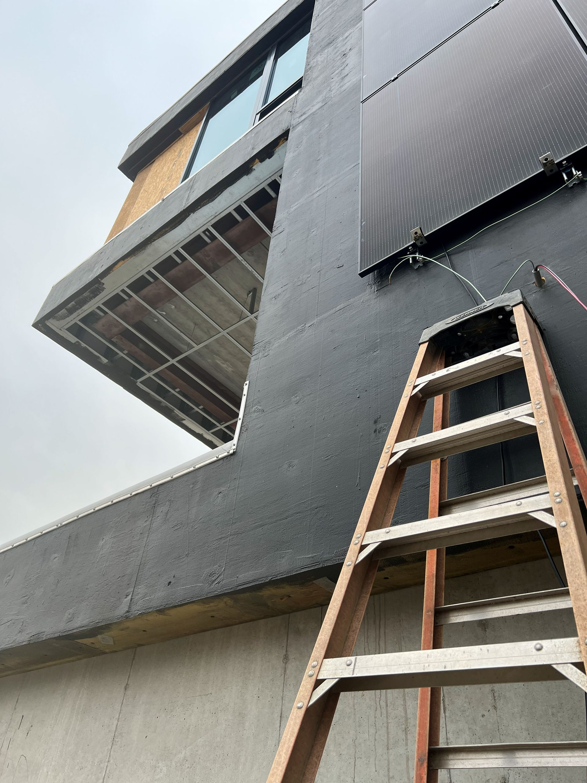 Ladder leaning against a dark-walled building with solar panels. Construction in progress.