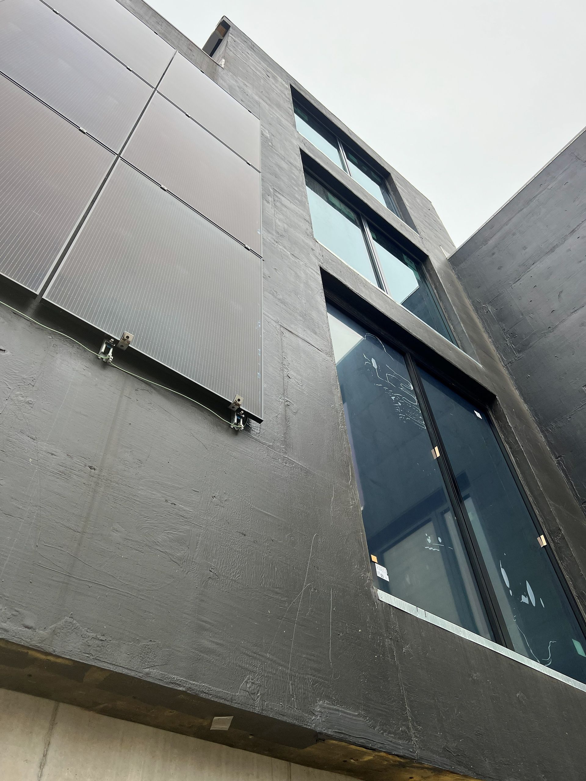 Dark-colored modern building with large windows and solar panels on the exterior.
