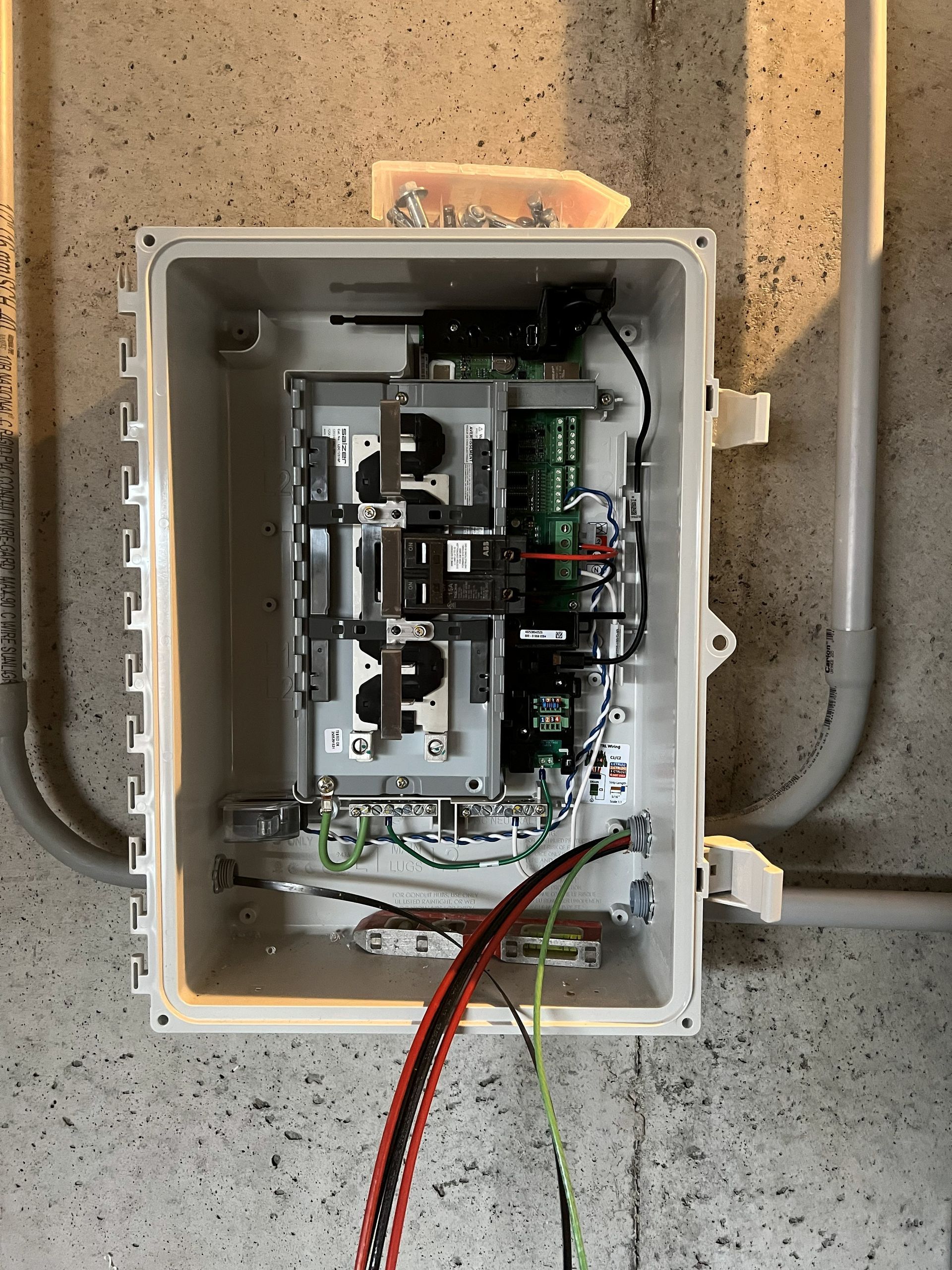Open electrical box on a wall, containing circuit boards, wires, and a terminal block.