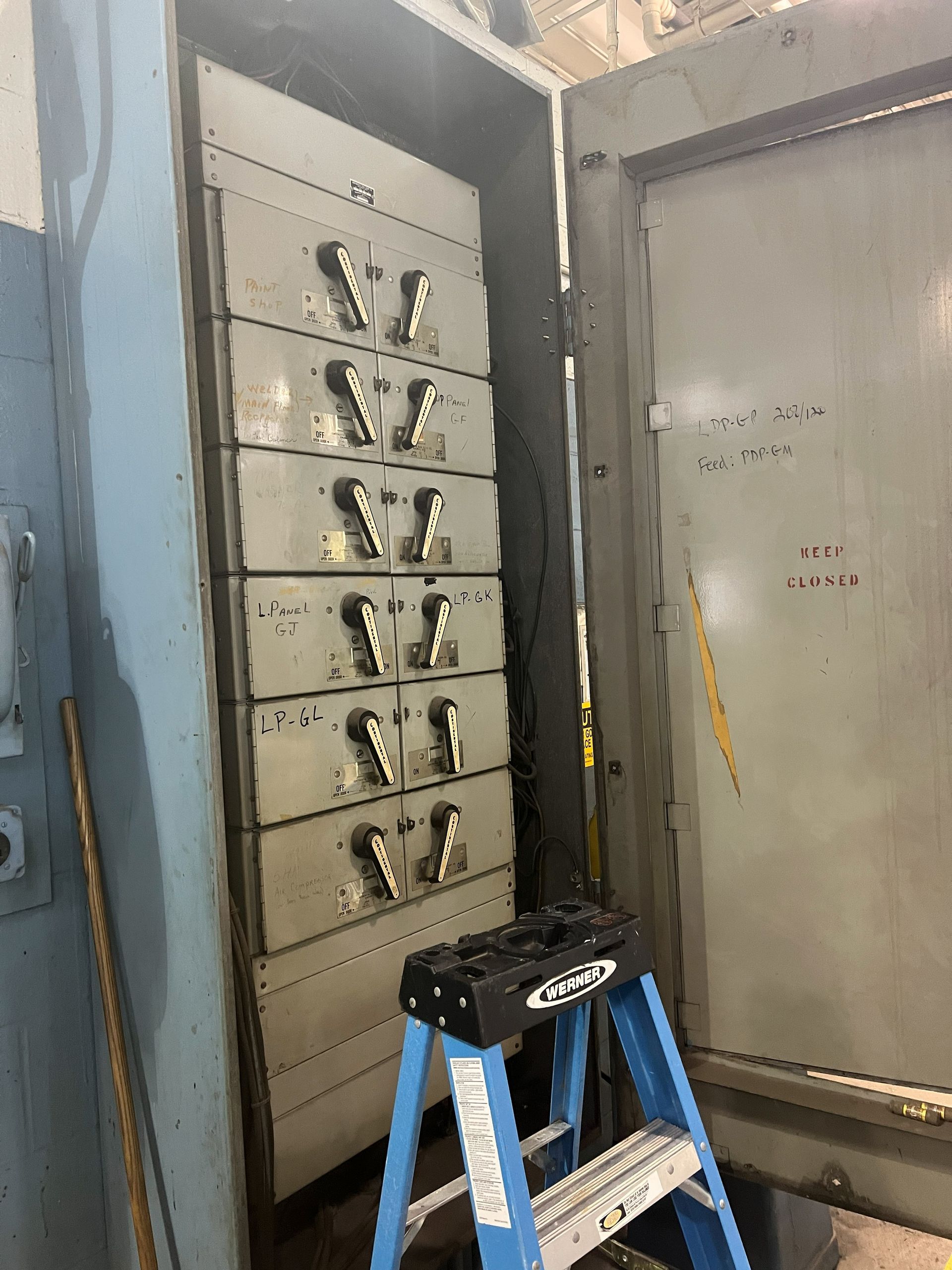 Metal electrical panel with multiple stacked compartments, open door, blue ladder.