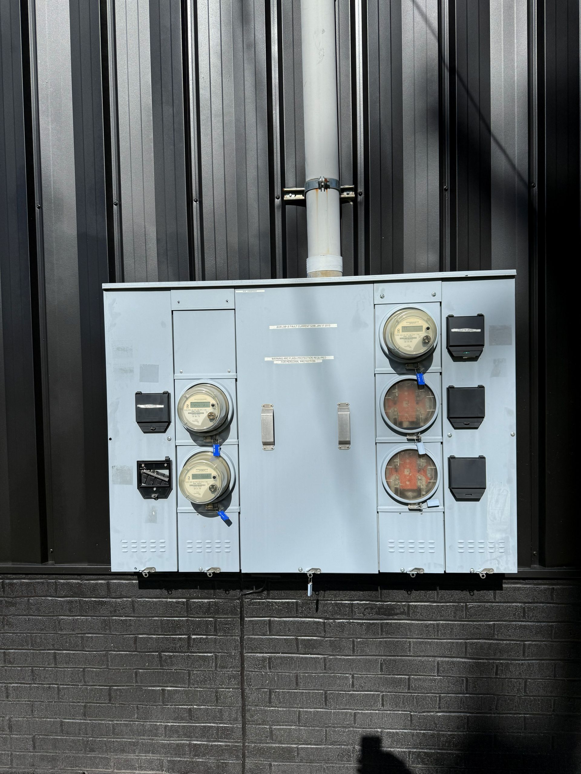 Gray electrical panel on a dark metal wall with several meters and outlets.