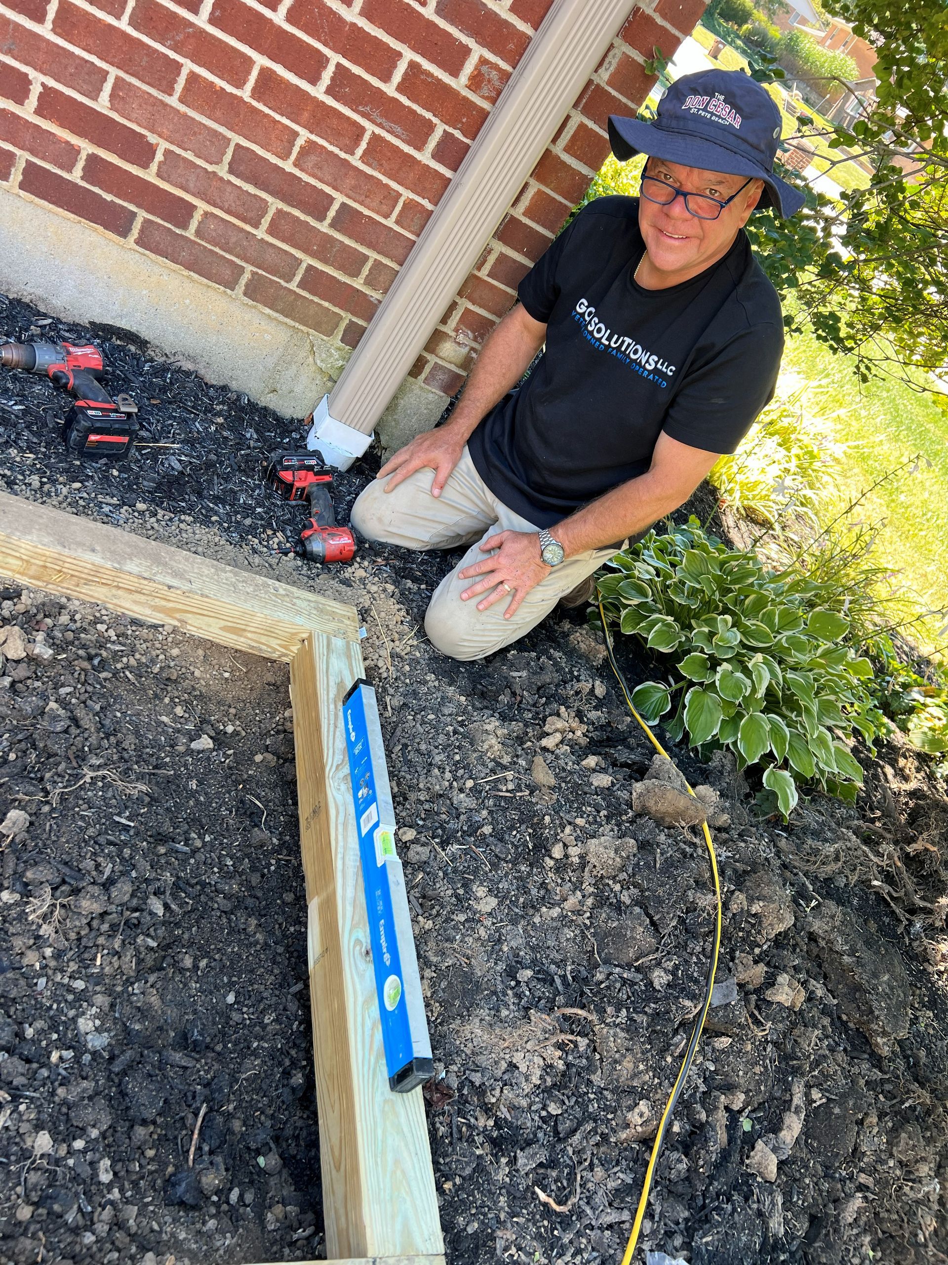 Man kneeling, using a level on a wooden frame next to a brick building.