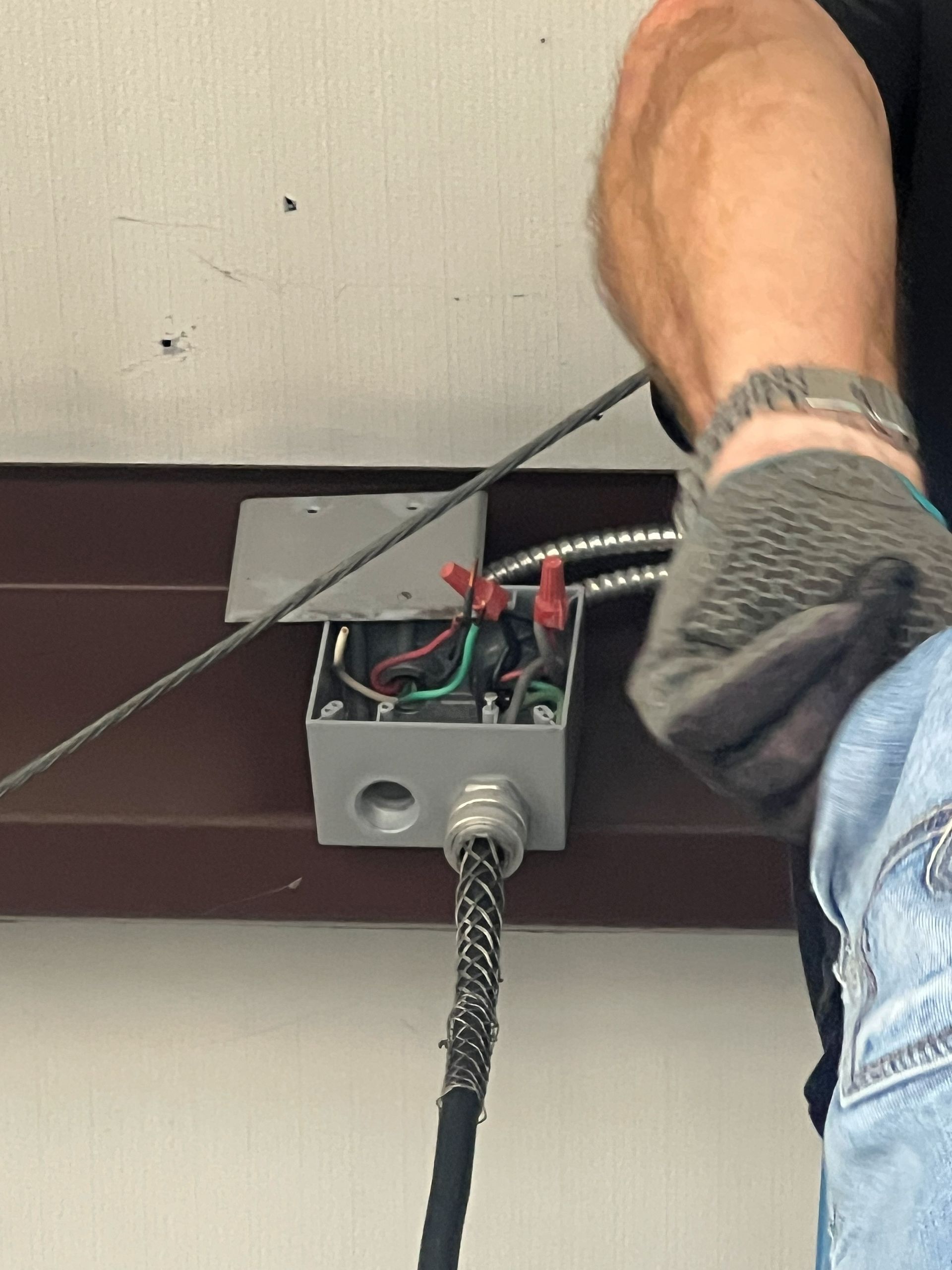 Person wearing gloves working on electrical wiring in a metal box.