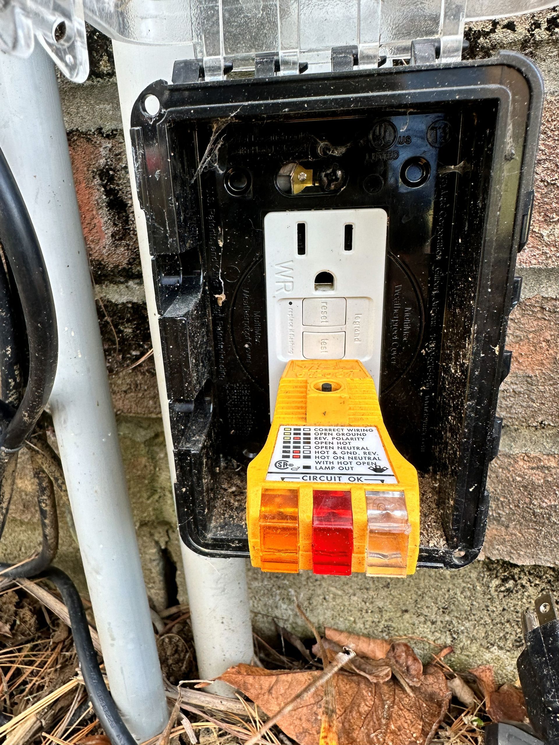 Yellow electrical outlet tester in an outdoor, weatherproof outlet box.