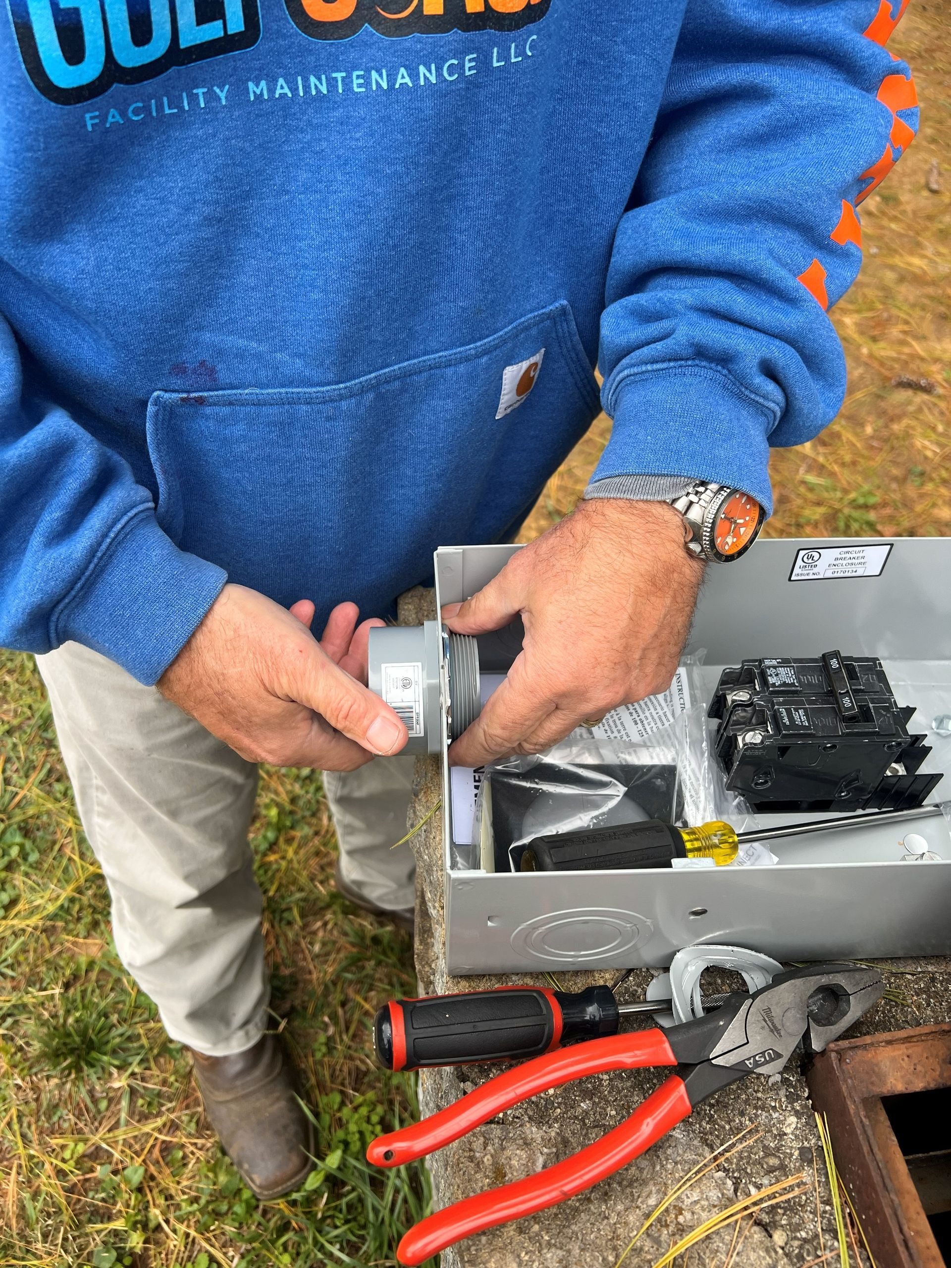 Person installing an electrical component in a metal box outdoors, with tools visible.