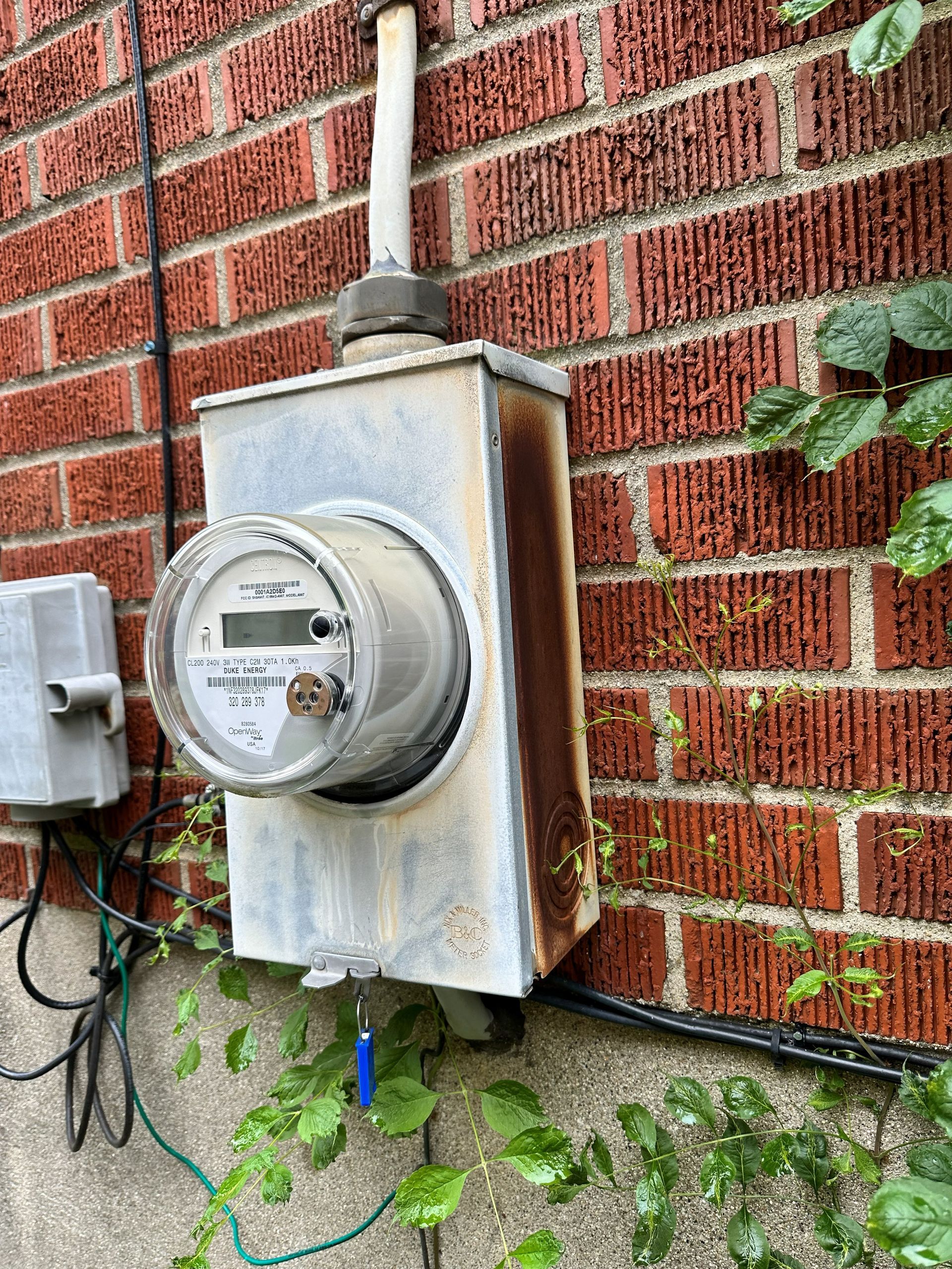 Electric meter on a brick wall with rusted metal casing and electrical wiring.