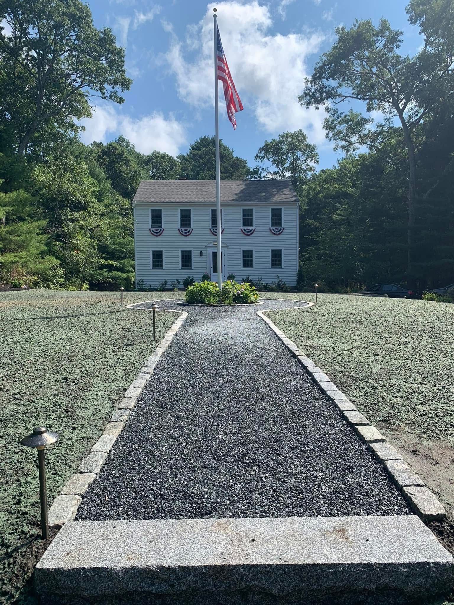 A gravel path leading to a house with an american flag on a pole.