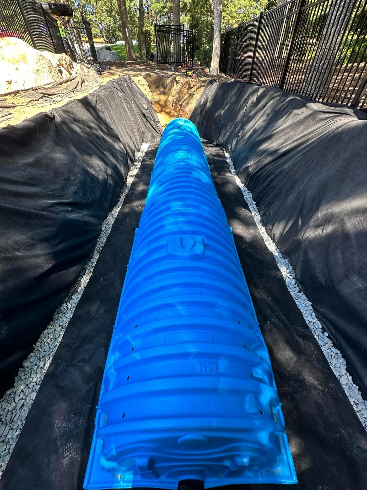A blue pipe is being installed in a trench.