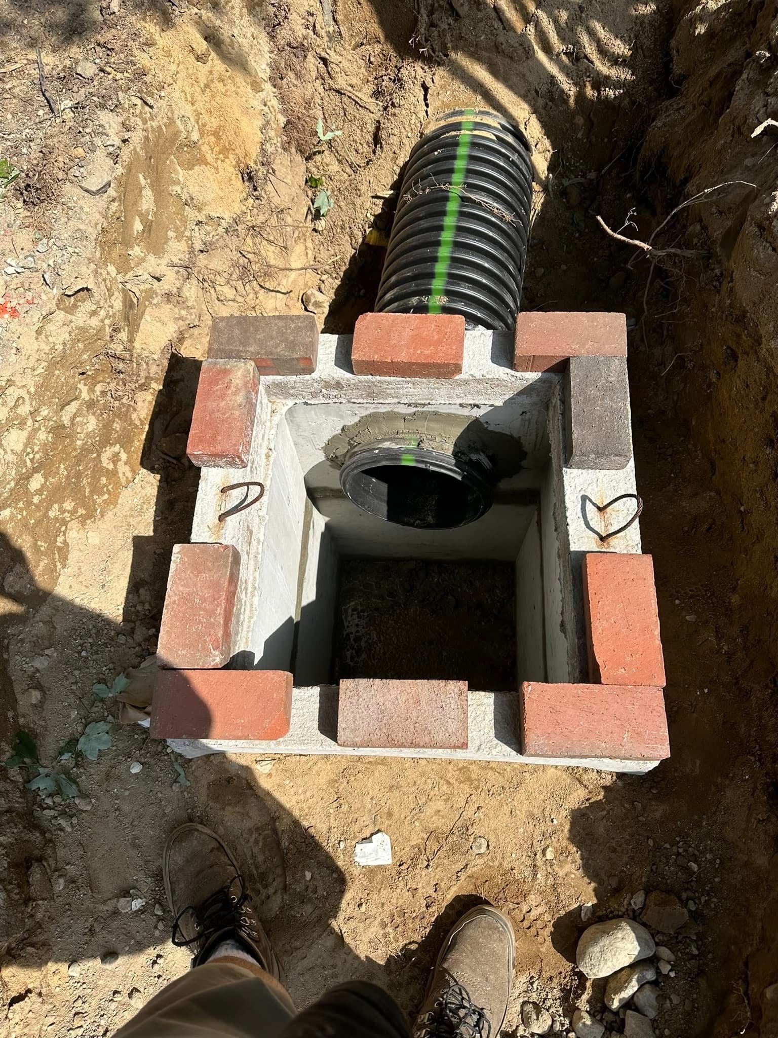 A person is standing in a hole in the ground next to a drain pipe.