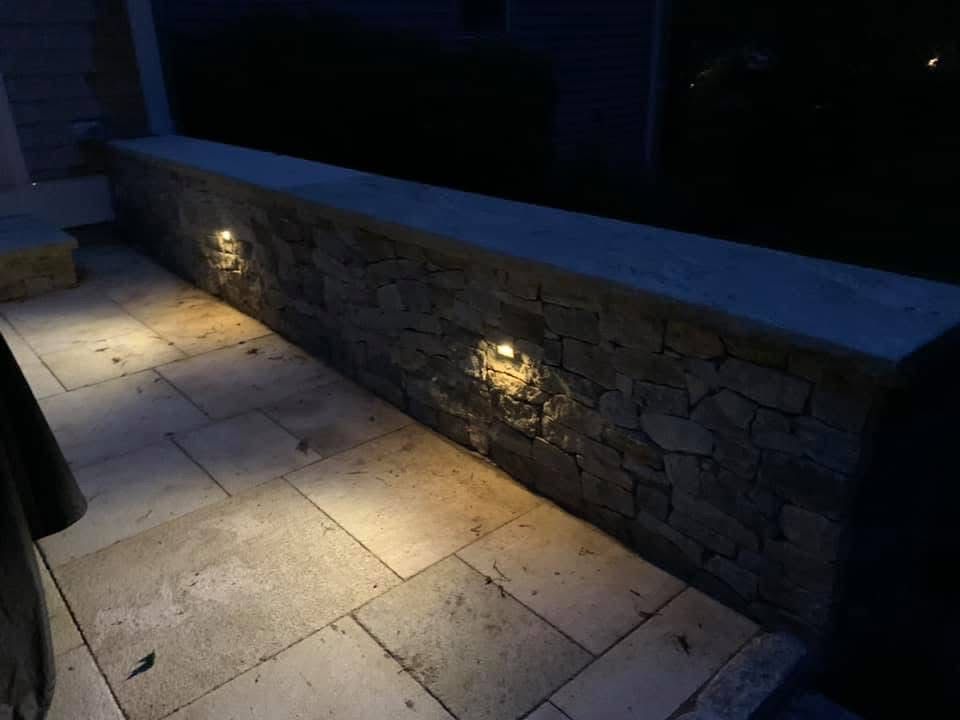 A stone wall with lights on it is lit up at night.