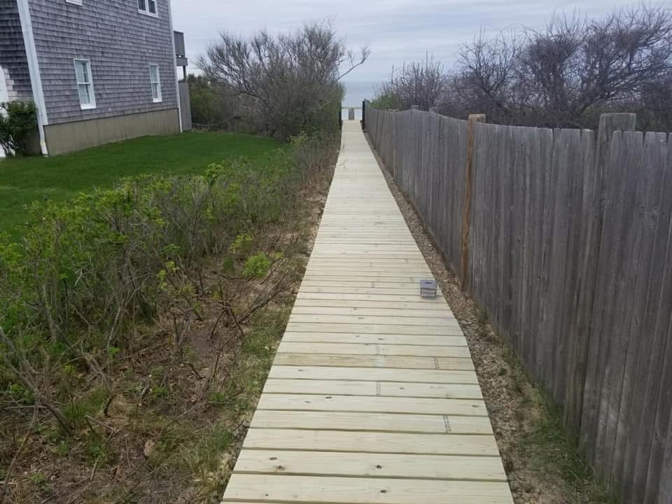 A wooden walkway leading to the beach with a fence in the background