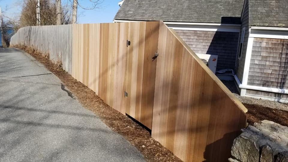 A wooden fence is along the side of a road next to a house.