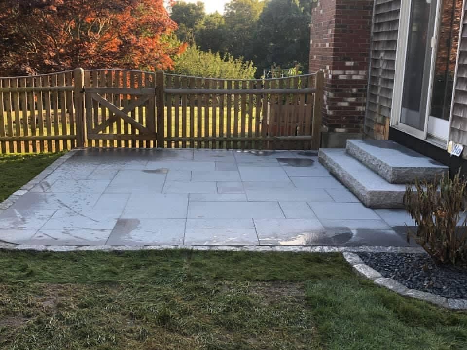 A patio with steps and a wooden fence in the backyard of a house.