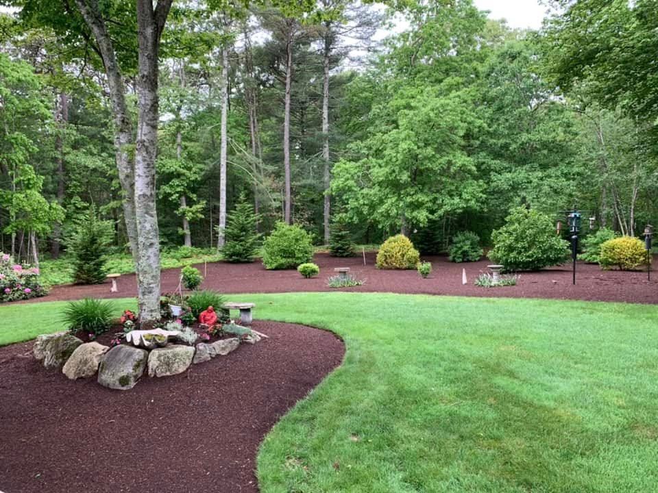 A lush green lawn with trees and rocks in the background