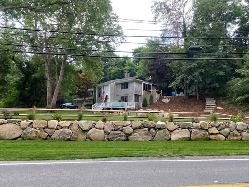 A stone wall along the side of a road with a house in the background.