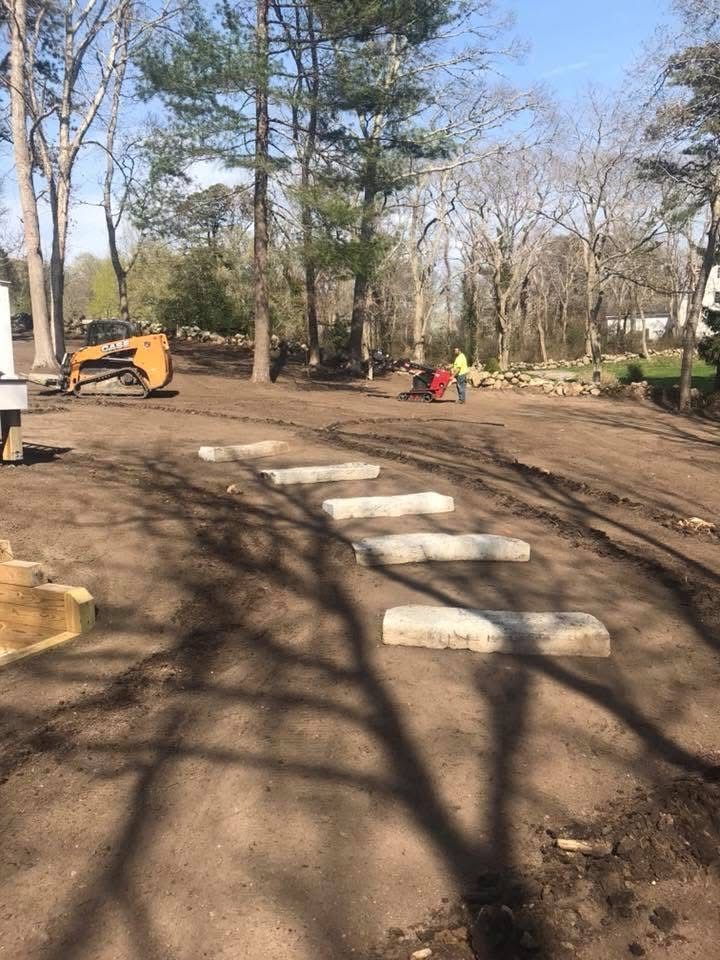 A group of people are standing in a dirt field with trees in the background.