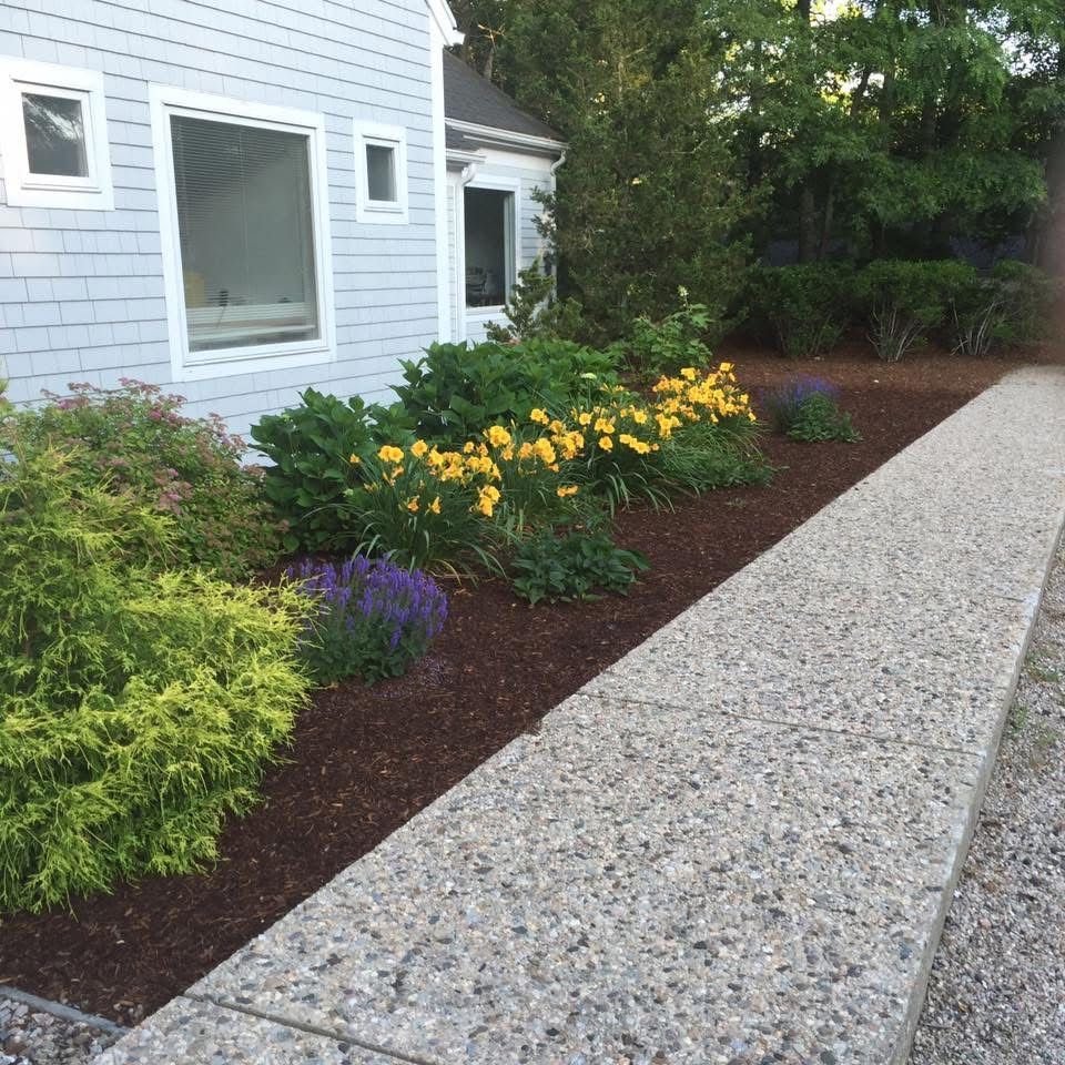 A walkway leading to a house with flowers in front of it