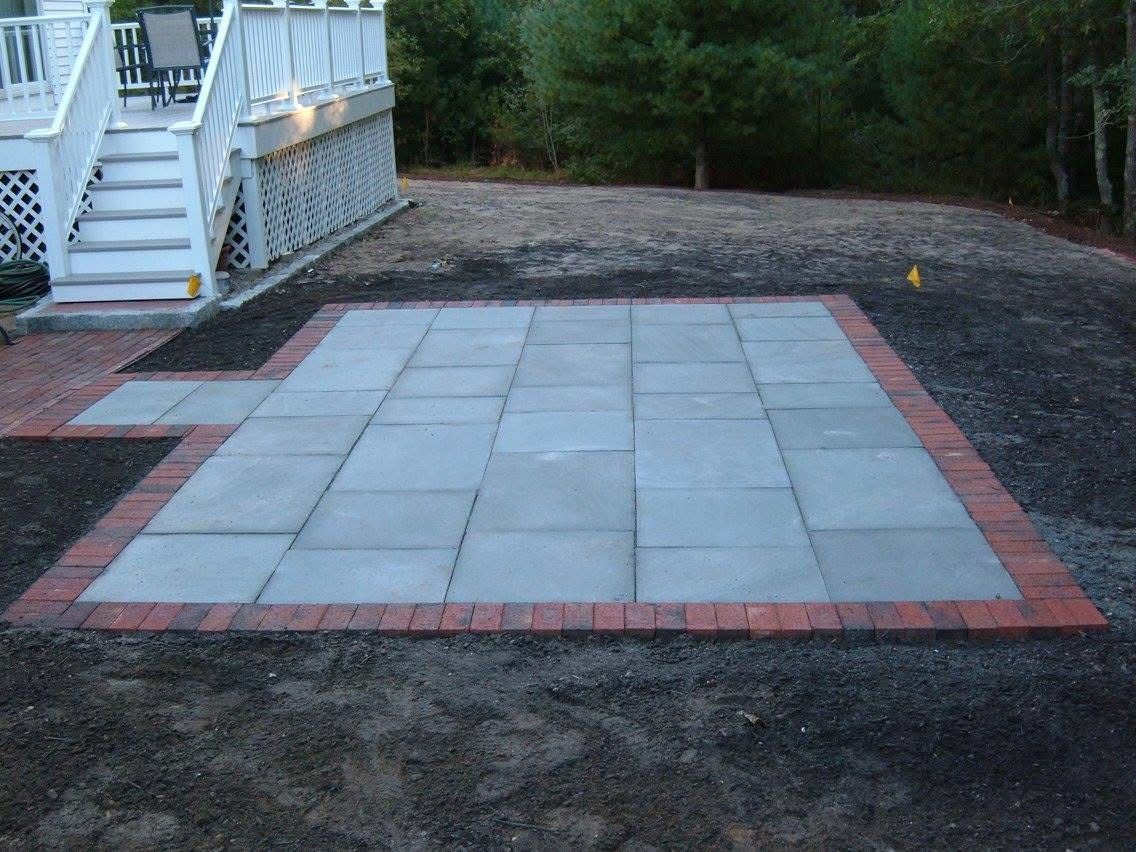 A patio with a brick border and a white deck in the background.