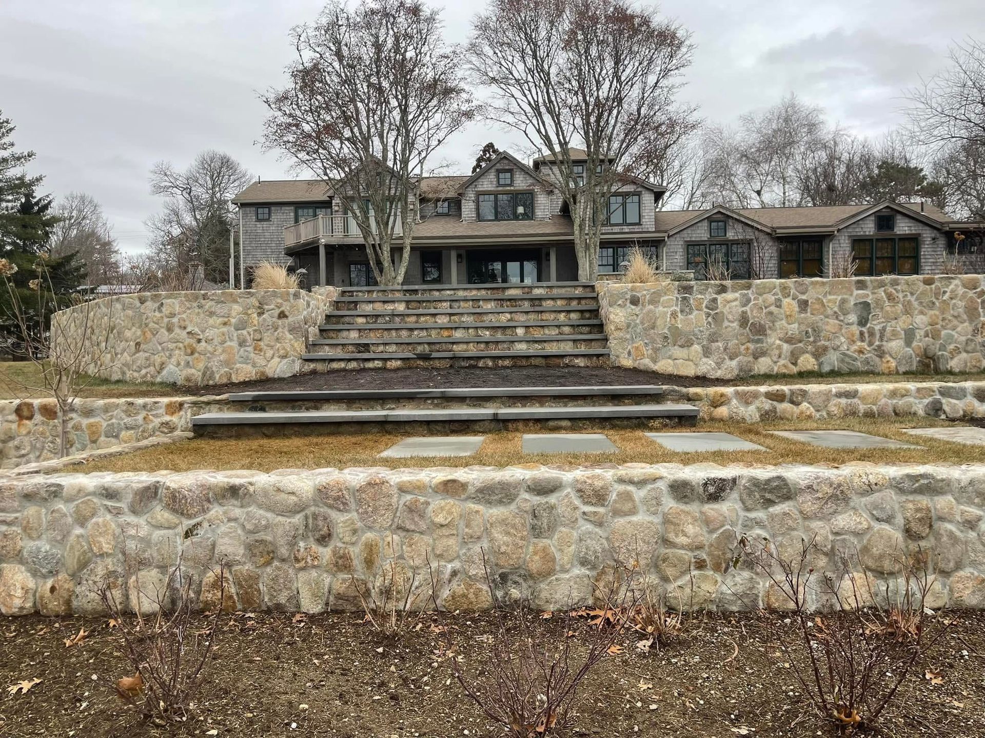 A large house with a stone wall and stairs in front of it.
