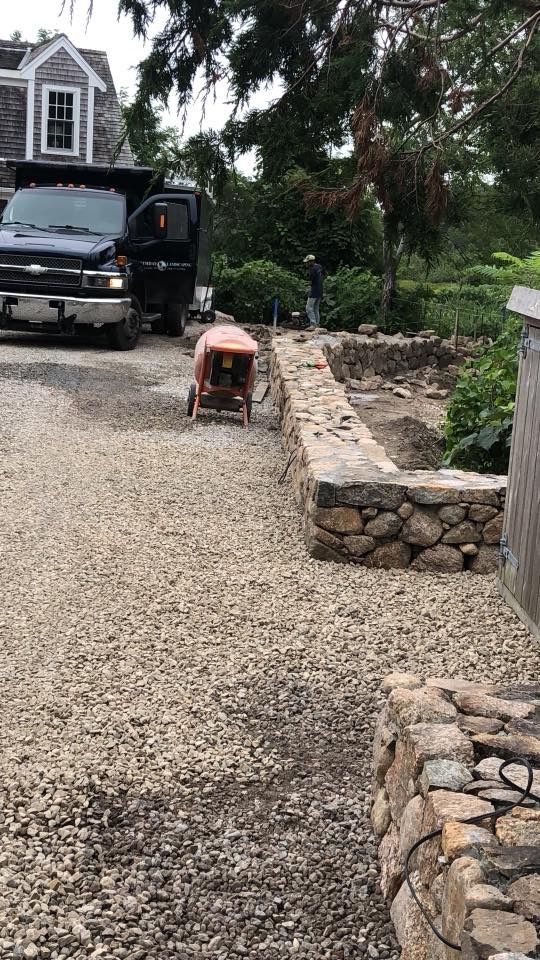 A truck is parked in a gravel driveway next to a stone wall.