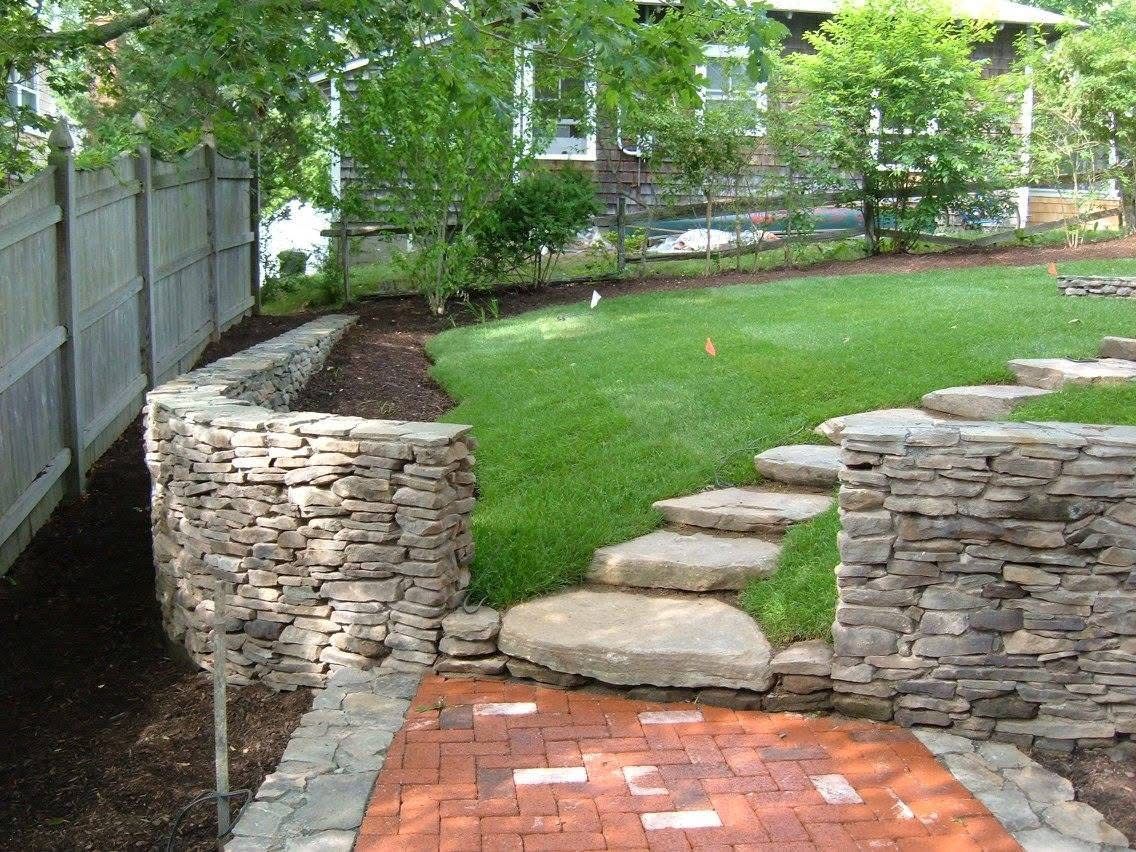 A backyard with a stone wall and brick walkway