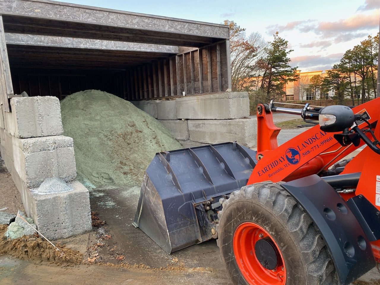 A tractor is loading a pile of concrete blocks into a shed.