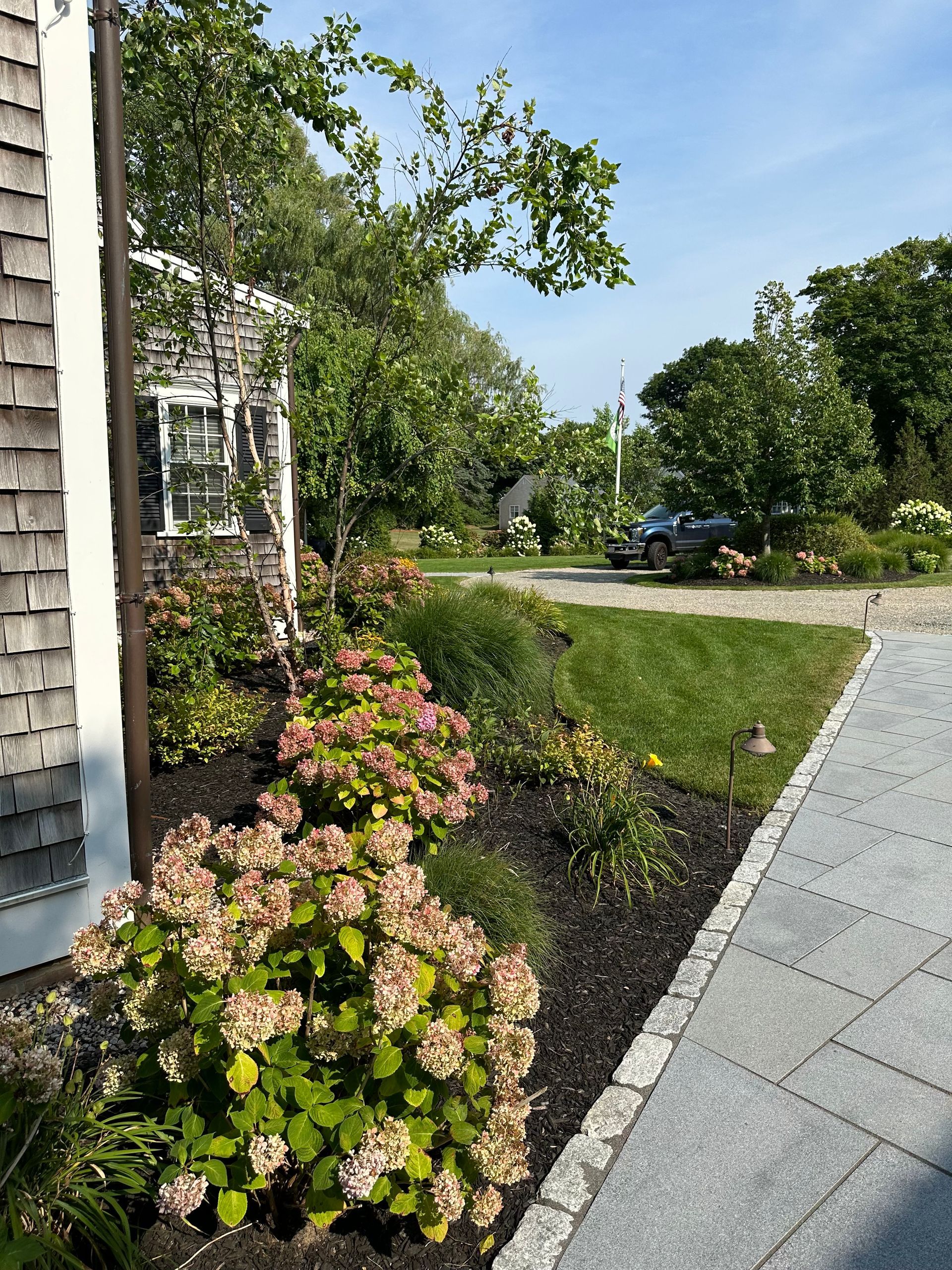 A sidewalk leading to a house with flowers and a driveway.