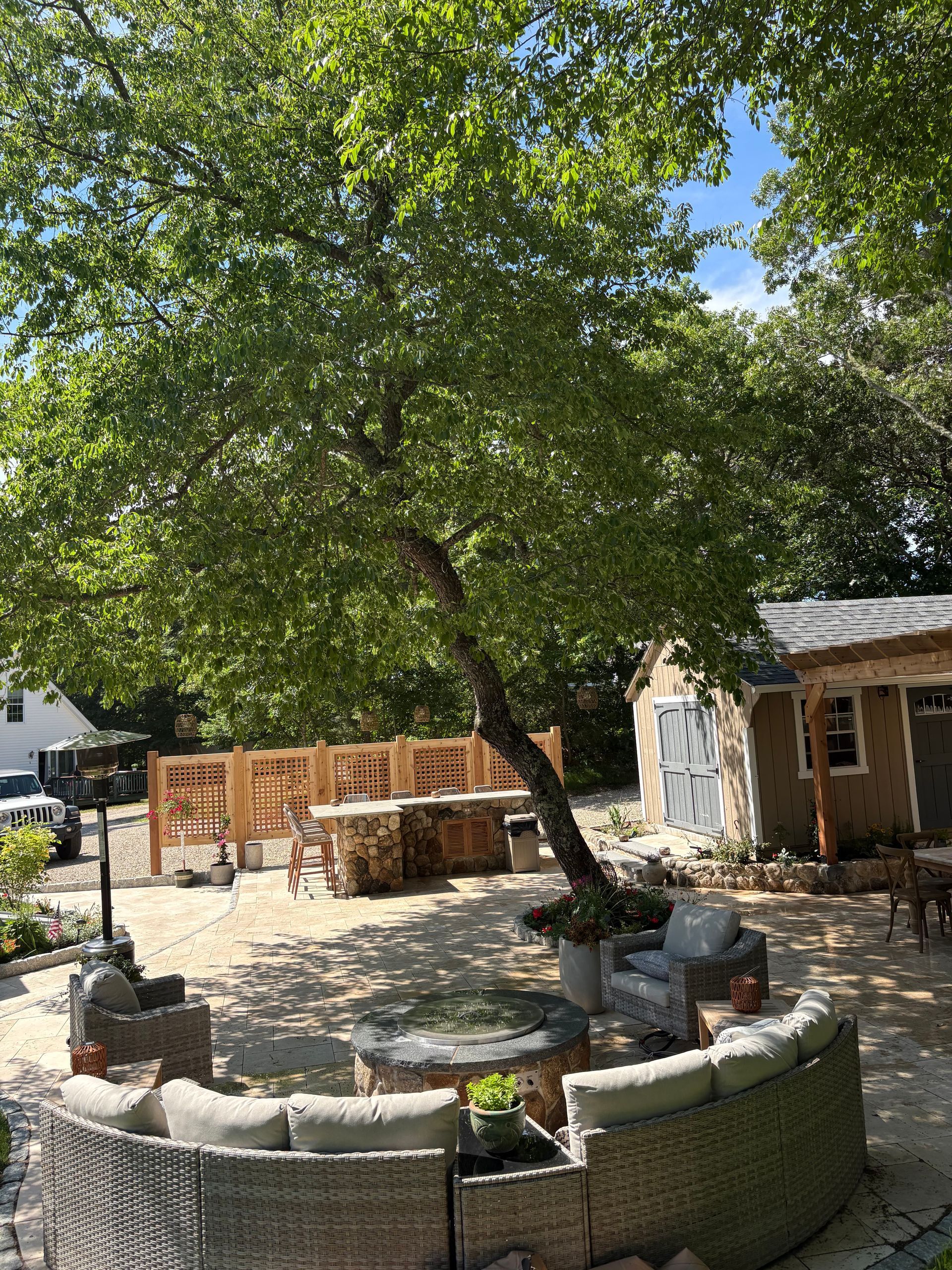 Courtyard with a large leafy tree, stone planter, and a small rustic building in the background