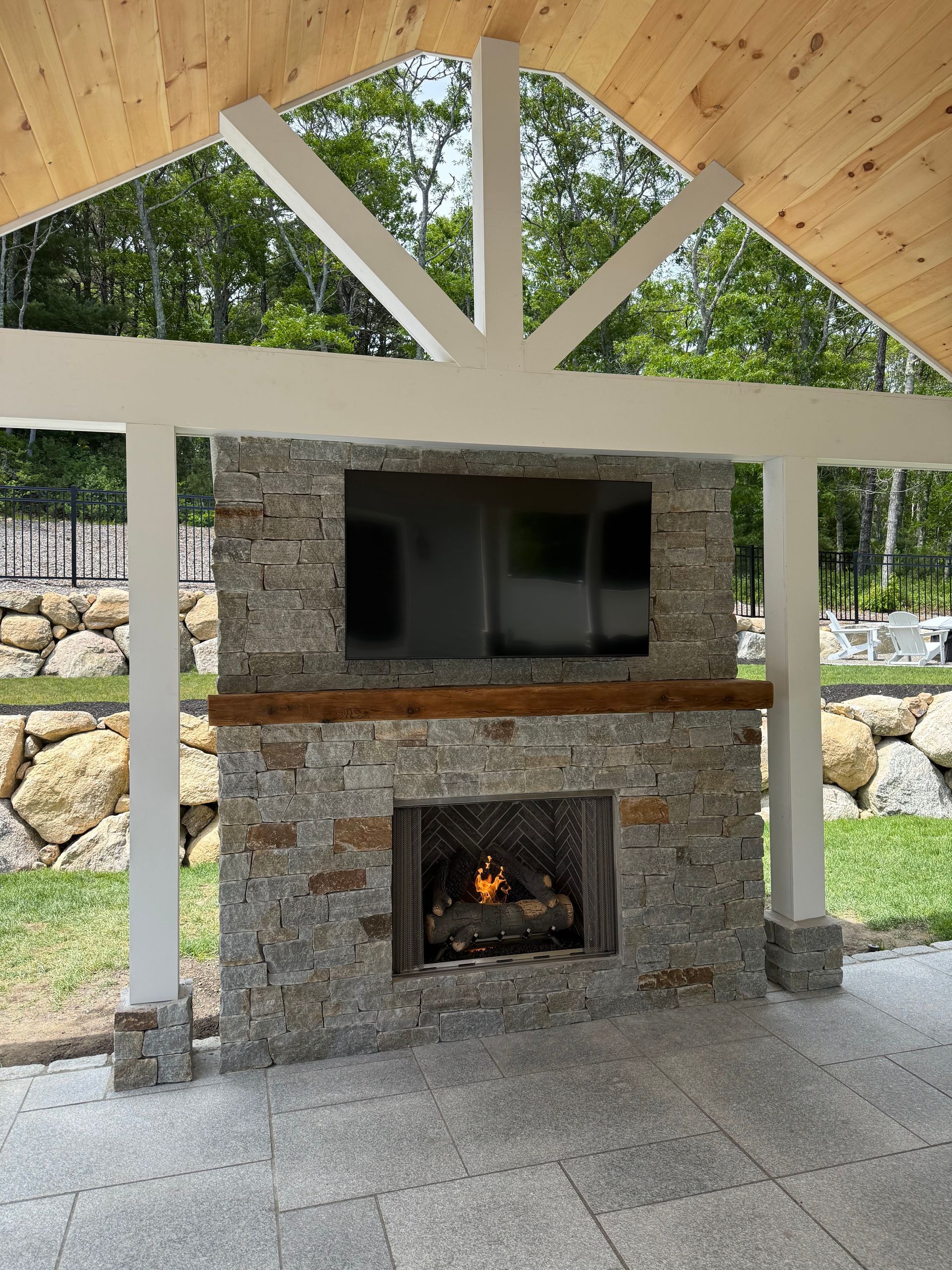Outdoor stone fireplace under a wooden pavilion, with a small fire burning inside.