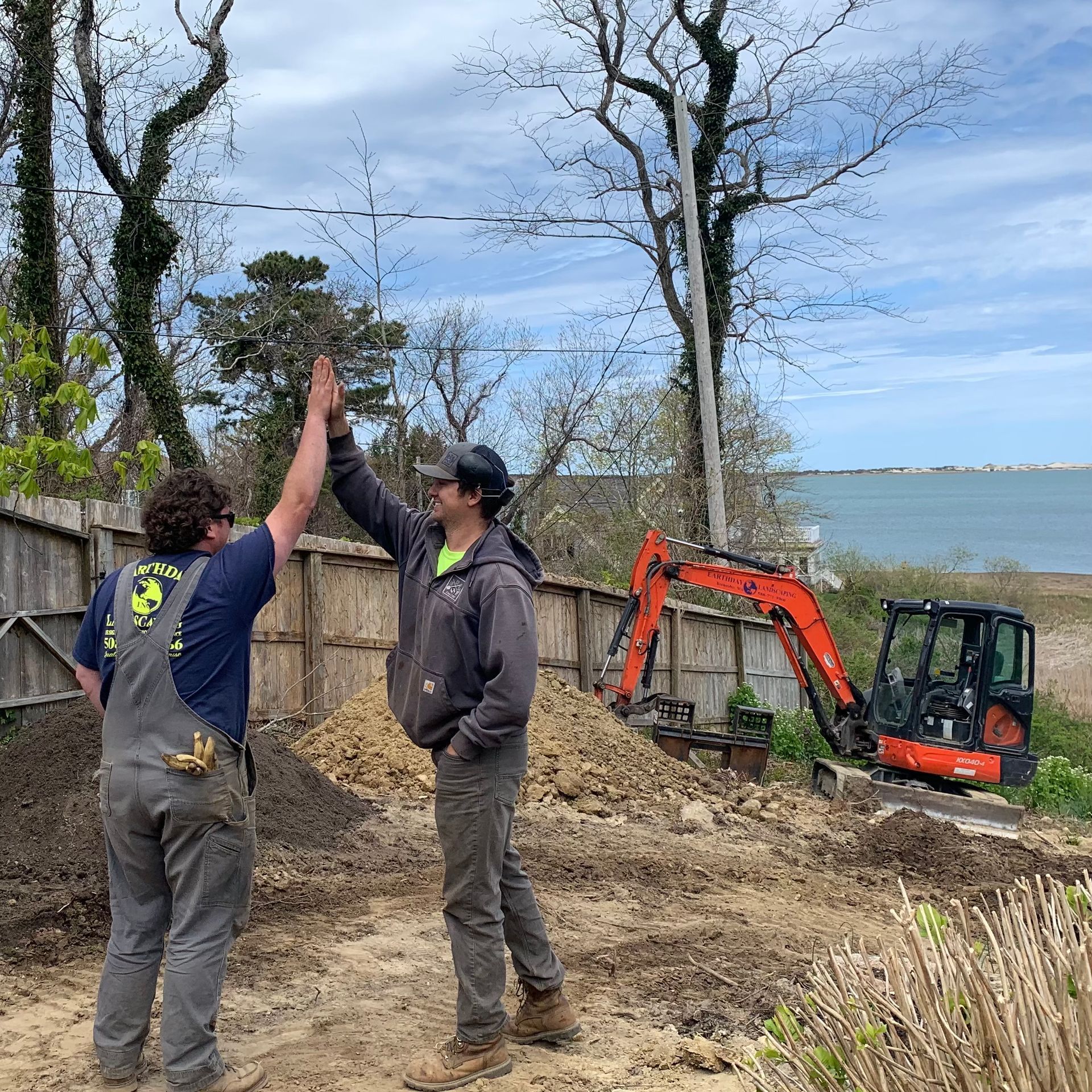 Two men are giving each other a high five in front of an excavator.
