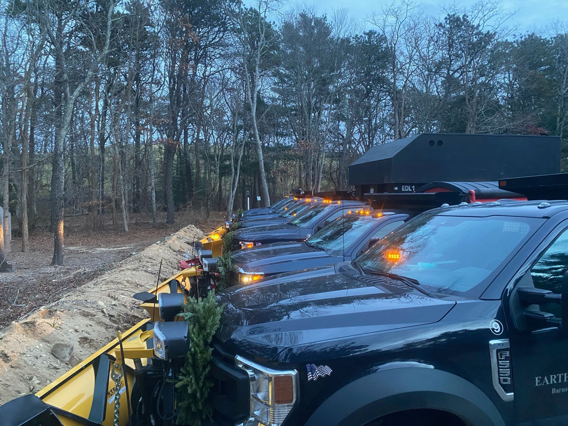 A row of black trucks parked next to each other on a dirt road.
