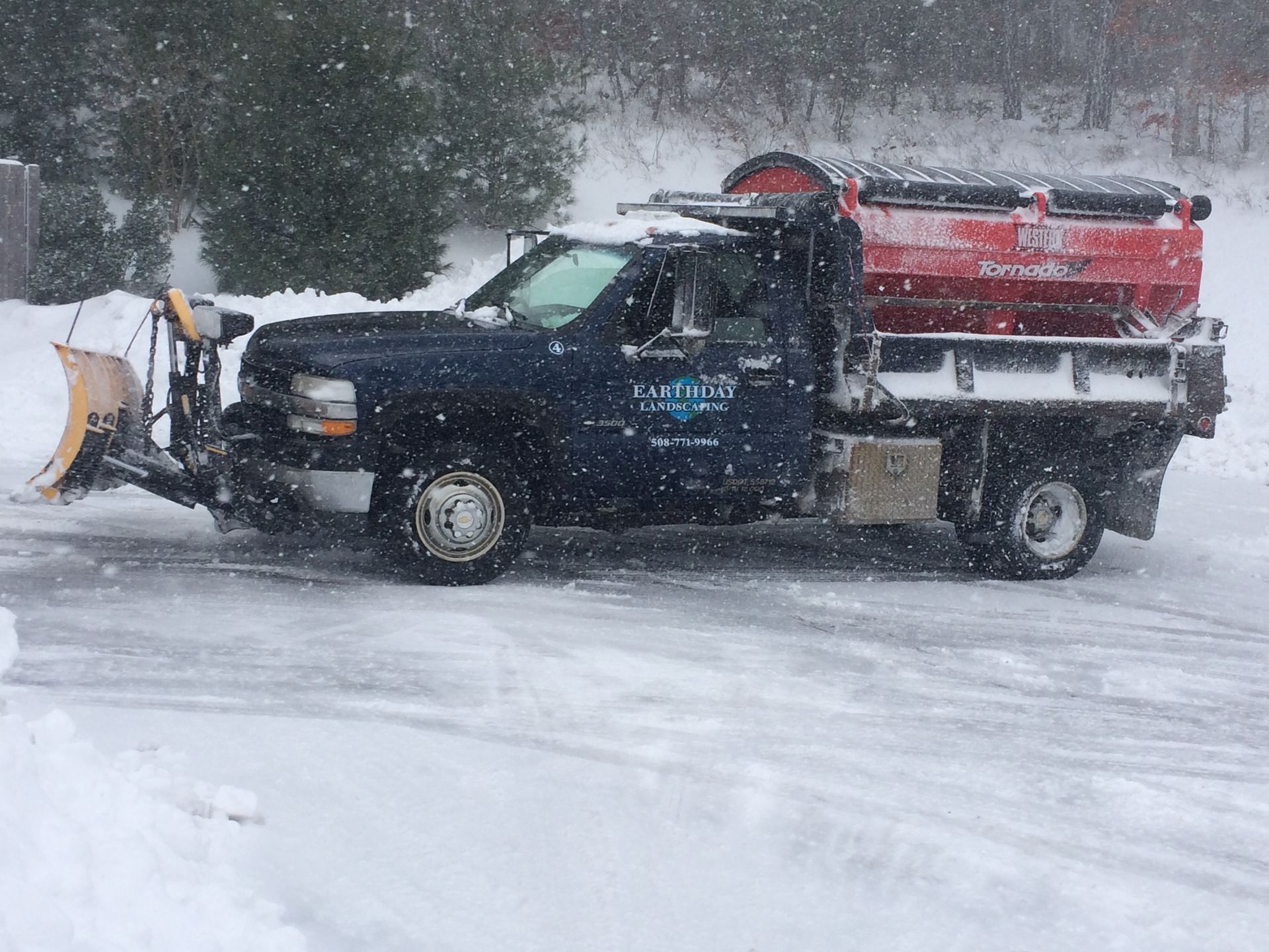 A snow plow is driving down a snowy road.