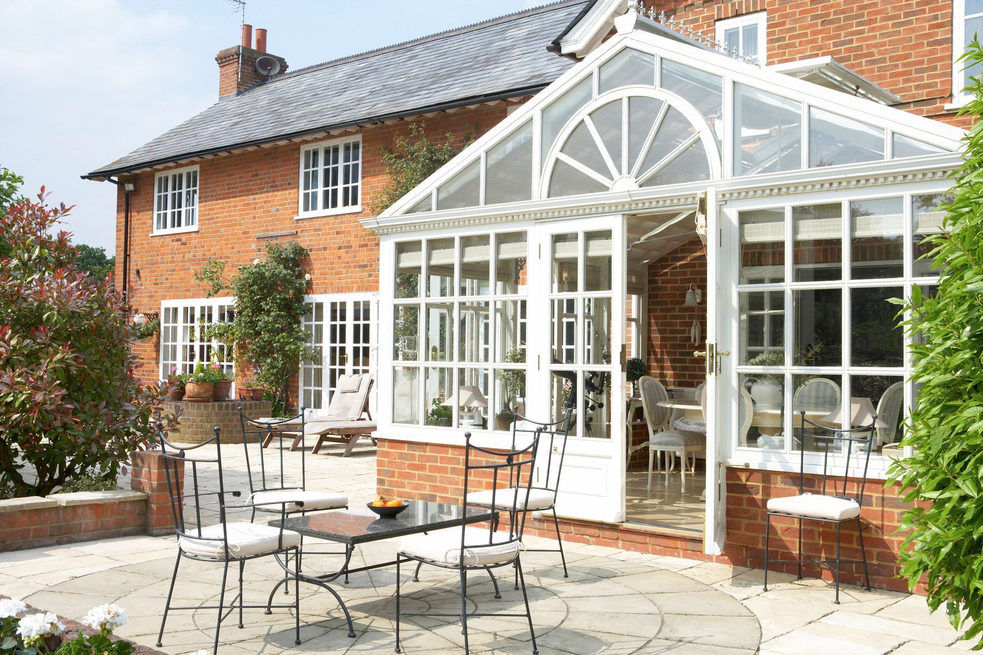 Brick house with white conservatory and patio furniture in a sunny garden